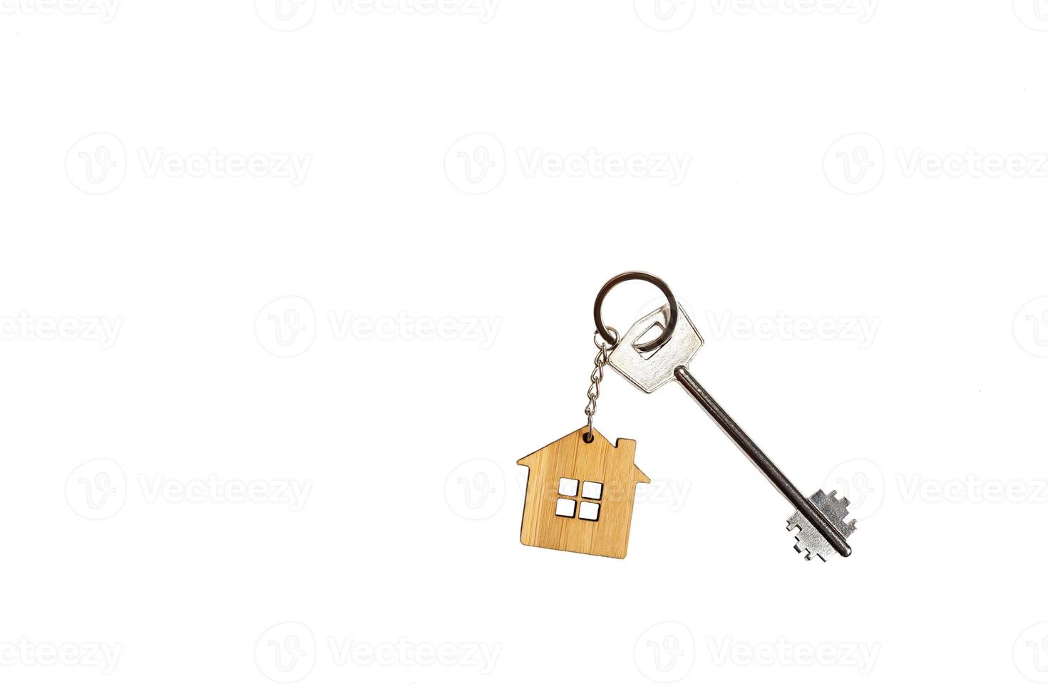 Key chain in the shape of wooden house with key on a white background, isolate. Building, design, project, moving to new home, mortgage, rent and purchase real estate, booking. Copy space photo