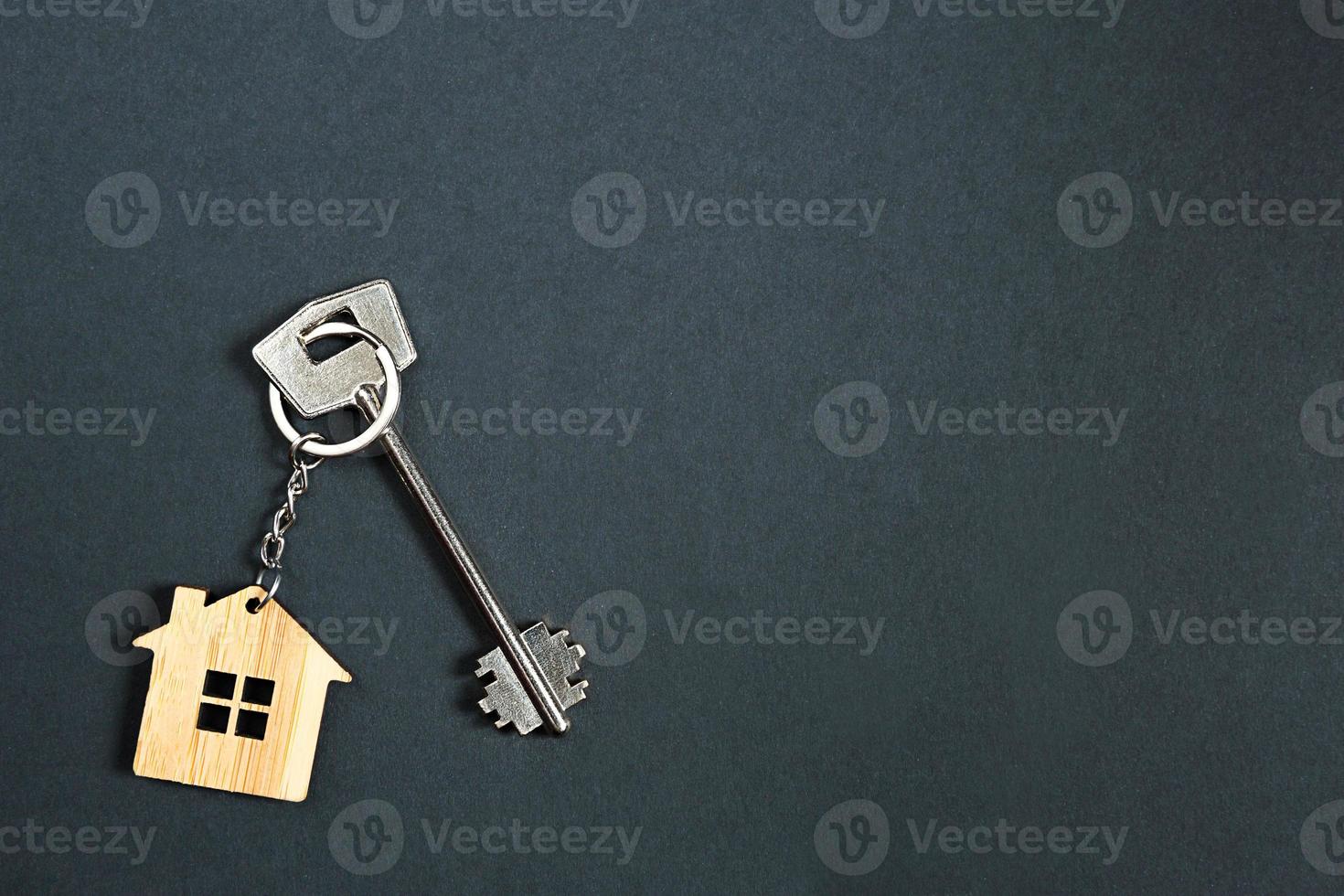 Key chain in the shape of wooden house with key on a black background. Building, design, project, moving to new home, mortgage, rent and purchase real estate. Copy space photo