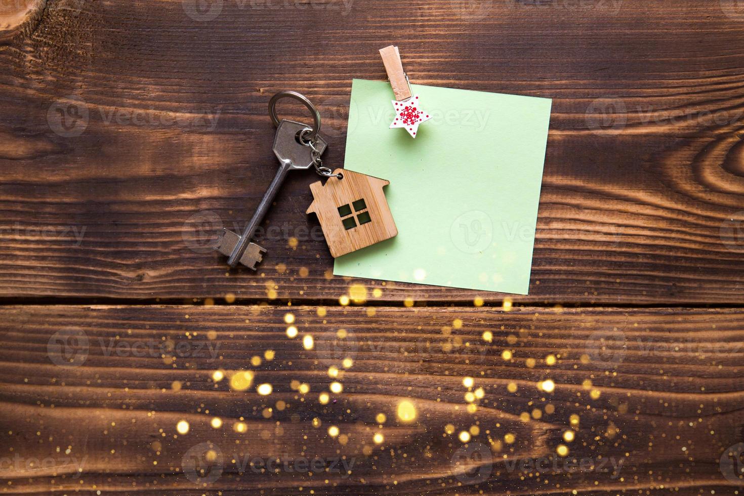House key with a keychain in the shape of a cottage on a wooden background on sheet notes with Christmas decor. Dream fulfillment, New year, transfer, shares of the mortgage, the rental of a cottage. photo