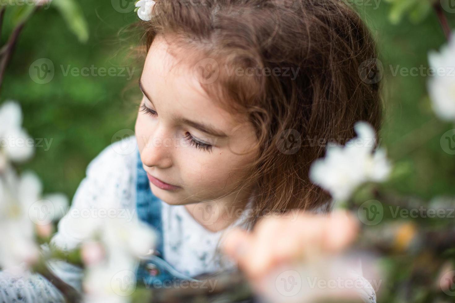 A cute little girl of 5 years old in a blooming white apple orchard in spring. Springtime, orchard, flowering, allergy, spring fragrance, tenderness, caring for nature. Portrait photo