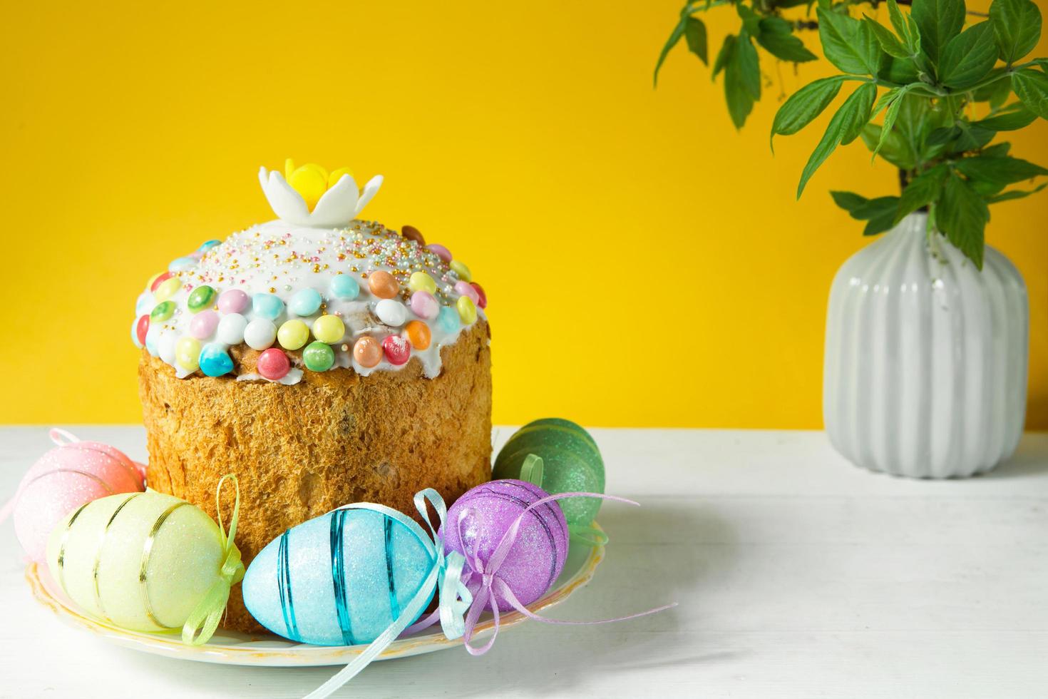 Easter cake with painted eggs on a platter in a white table. Traditional festive food. Yellow background photo