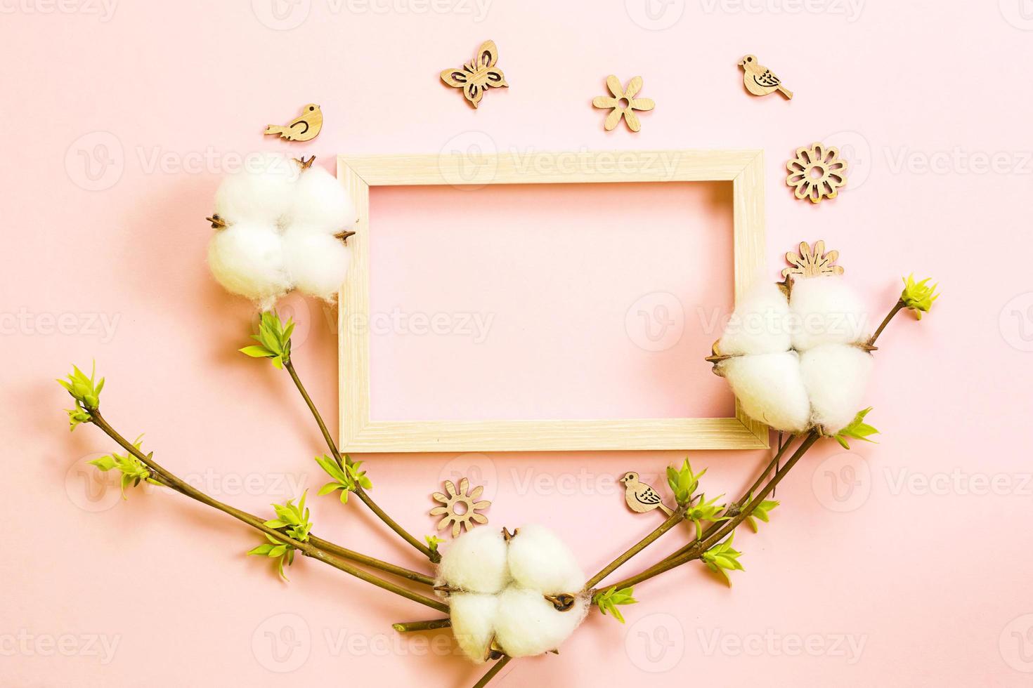 Frame made of cotton flowers, delicate little leaves from open buds on branches-sprouts on a pink background and carved wood butterflies, birds, ornaments. Spring, new life, tenderness. Copy space photo