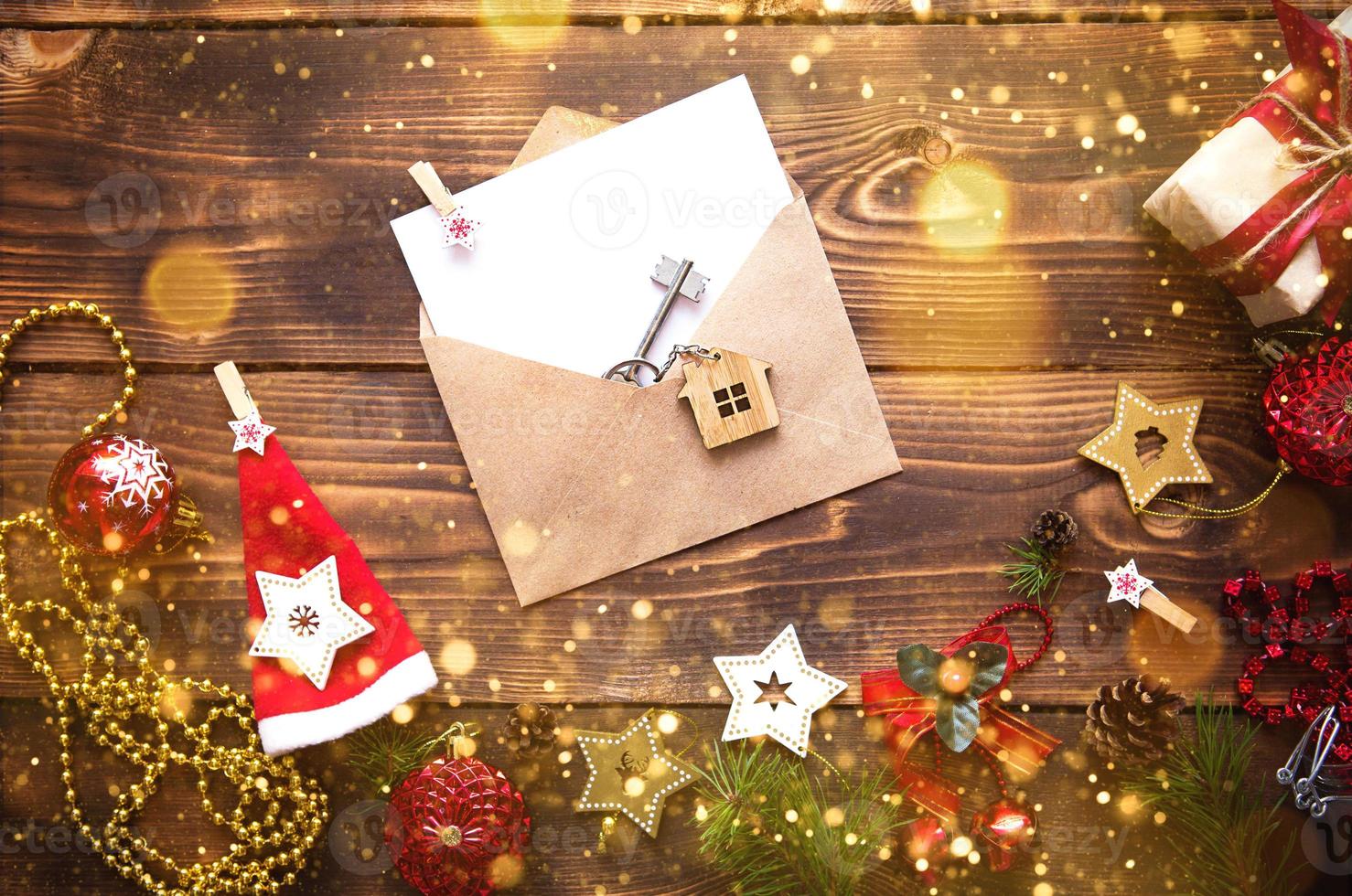 Christmas flat lay on a wooden background with keys to new house in the center with a envelope with a note sheet. New year, transfer, shares of the mortgage, the rental of a cottage. Space for text photo