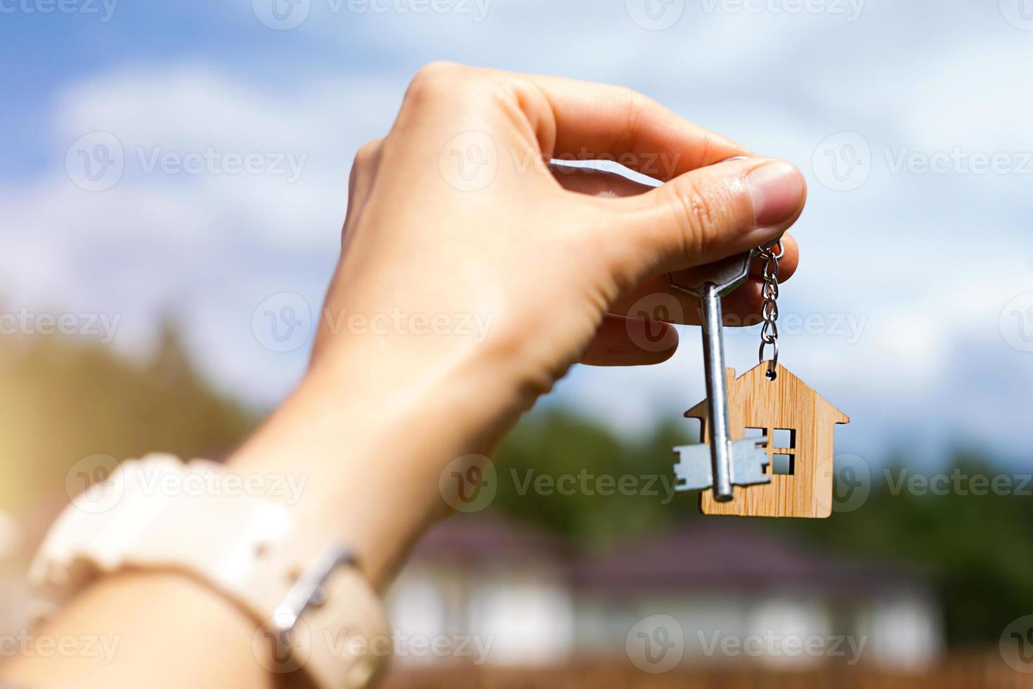 Wooden pendant of a house and key. Background of countryside, nature. Dream of home, building, delivery of the project, moving to a new house, mortgage, rent and purchase real estate. Copy space photo