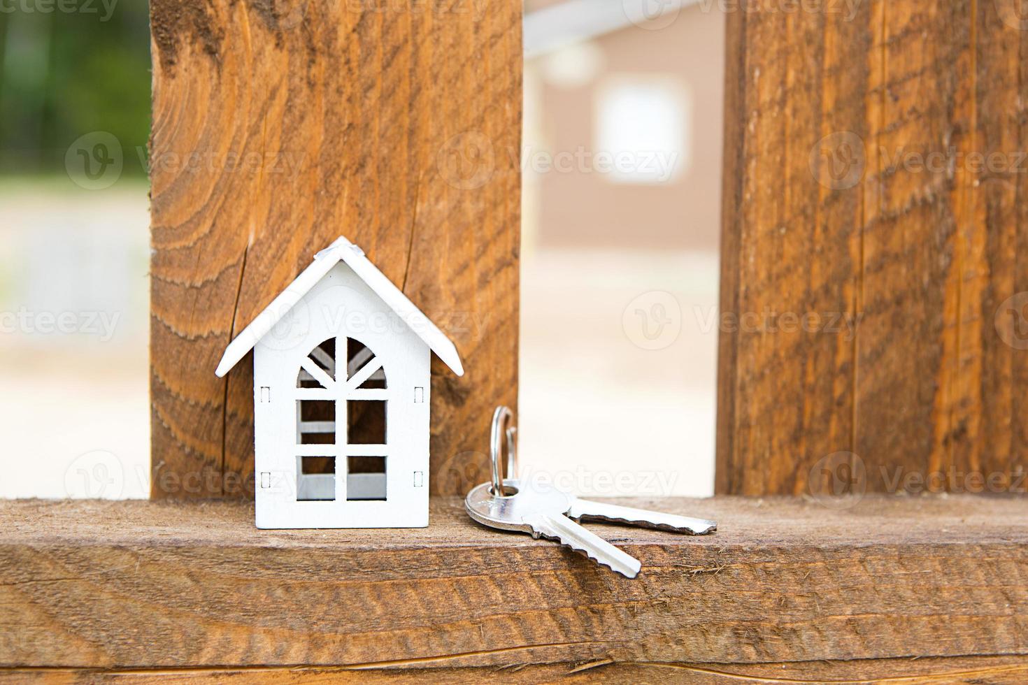 Small figure of white wooden house on fence with key to housing against the background of cottages. Building, design, project, moving to new house, mortgage, rent and purchase real estate. Copy space photo
