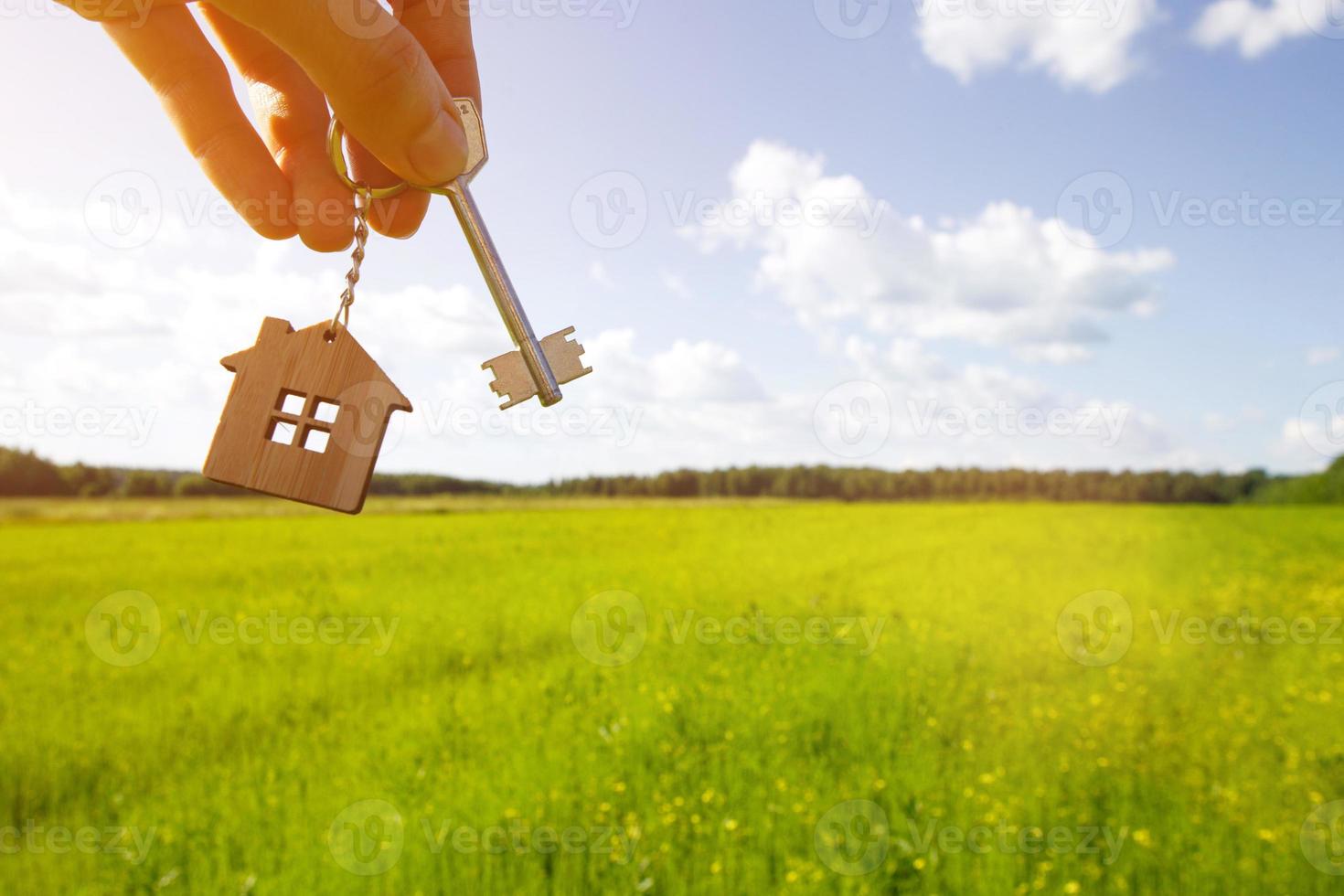 colgante de madera de una casa y llave. fondo del cielo y el campo. sueño de casa, construir una casa de campo en el campo, plan y diseño, entrega del proyecto, mudanza a una nueva casa. copie el espacio foto