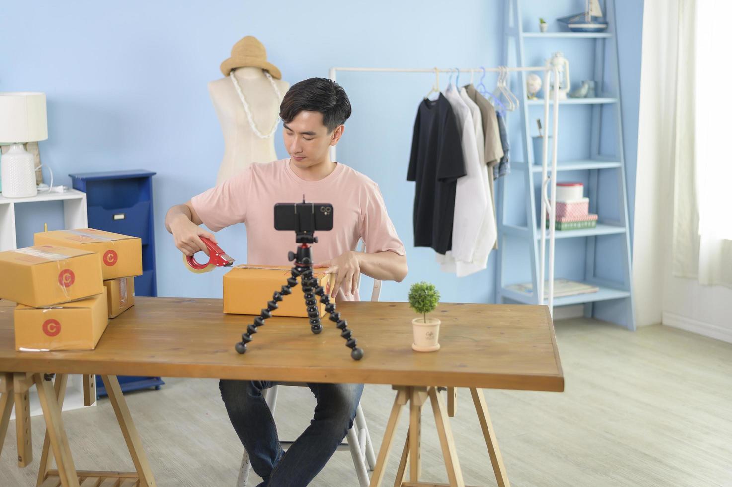 un hombre asiático está mostrando ropa frente a la transmisión en vivo de un teléfono inteligente en su tienda. concepto de negocio en línea de tecnología. foto