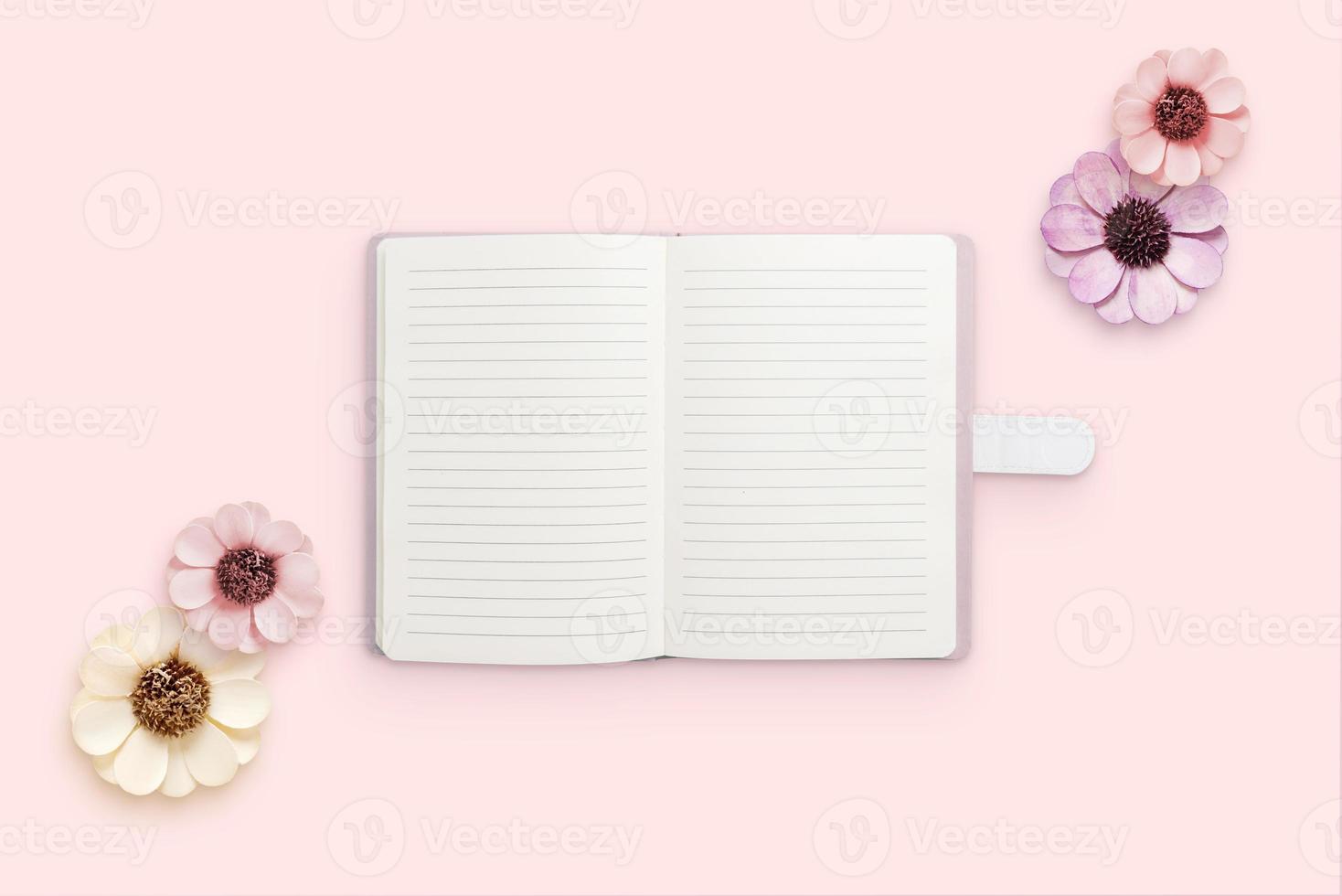 Notepad surrounded by flowers on pink surface. Blank papers for text. Flat lay, top view composition photo