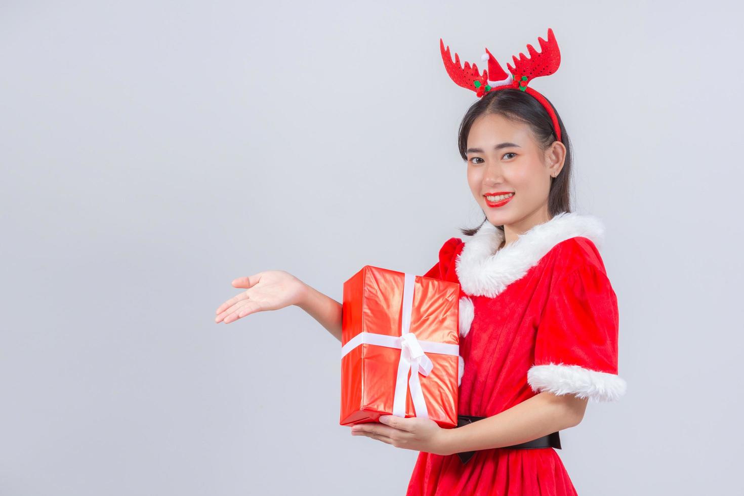 Chica asiática en vestido de Navidad con caja de regalo sobre fondo blanco. foto