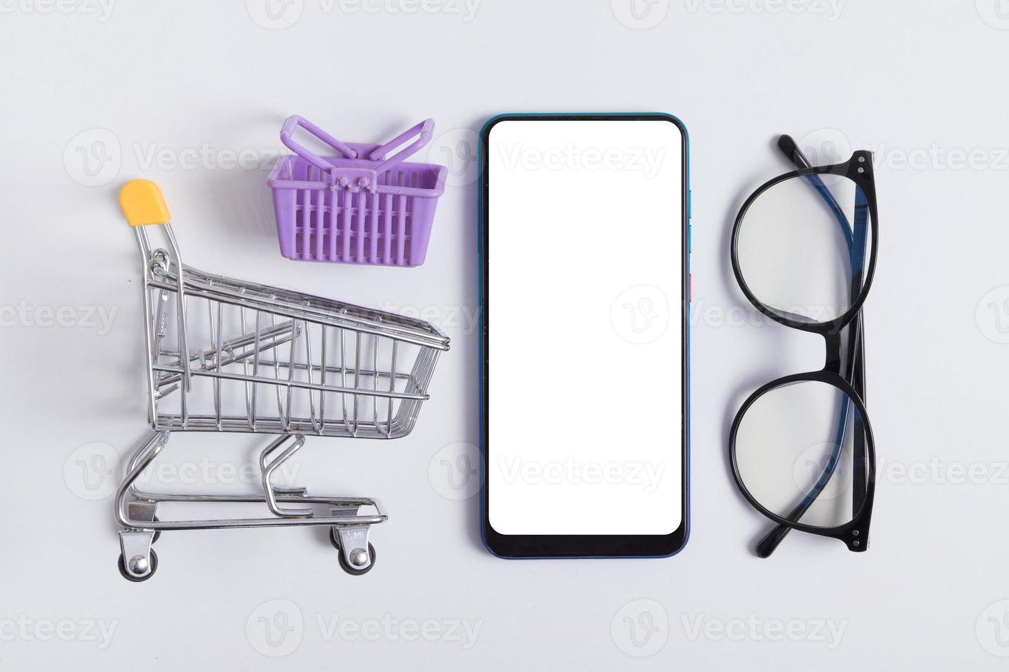 Online shopping flat lay creative composition. Knolling with phone mock up, supermarket trolley and glasses photo