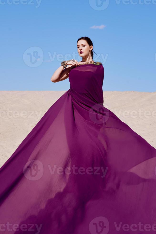 increíble hermosa mujer morena con la pluma de pavo real en tela púrpura en el desierto. oriental, indio, moda, concepto de estilo foto