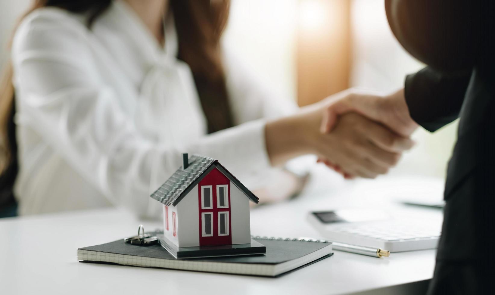 construction worker shaking hands with customer after finishing up business meeting to start up project contract in office center at construction site behind house model, home loan contract concept photo