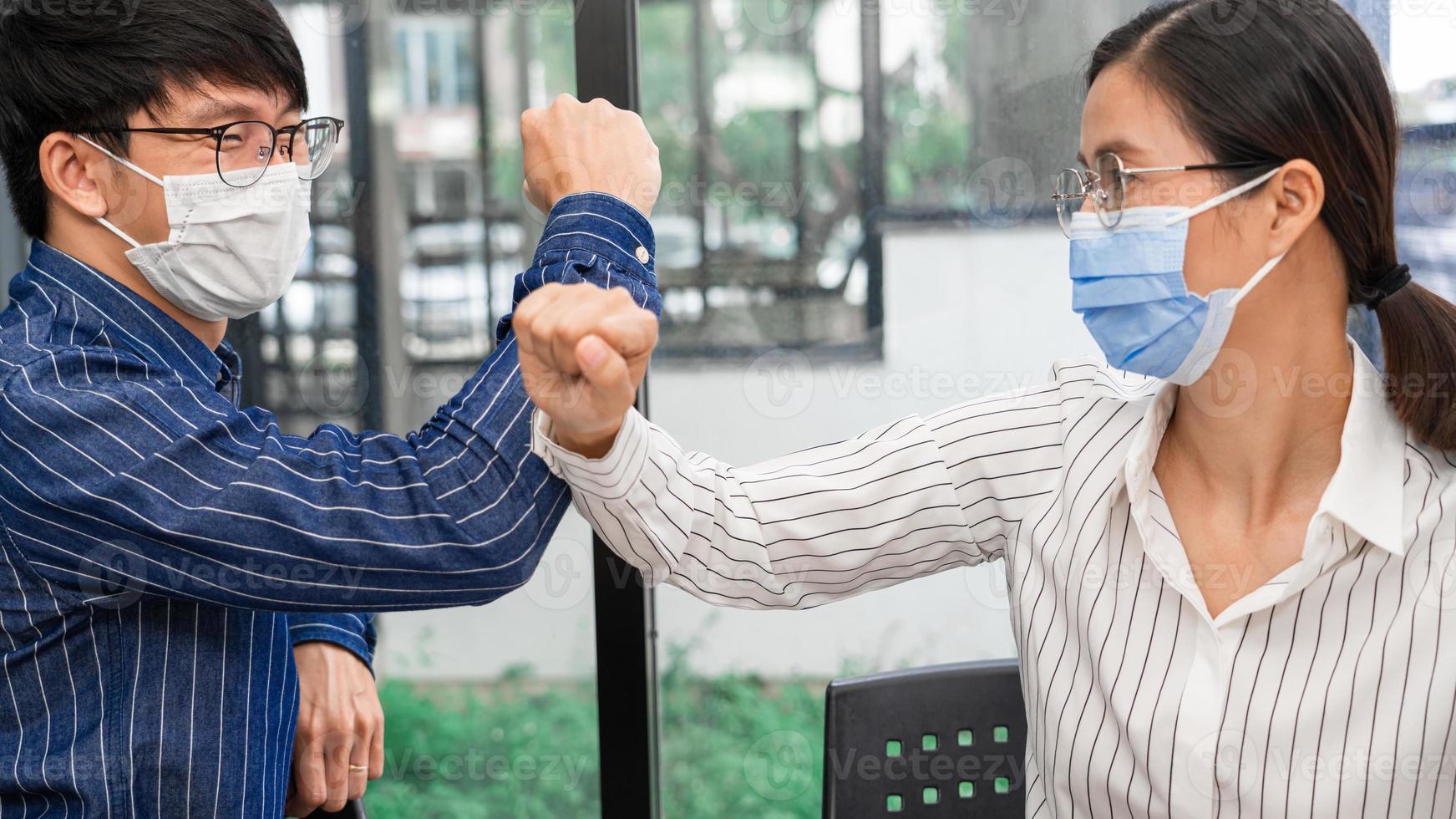 Two Asian colleagues in medical masks avoid a handshake when meeting in the office greeting with bumping elbows during coronavirus COVID-19 epidemic in office, Social distancing concept. photo