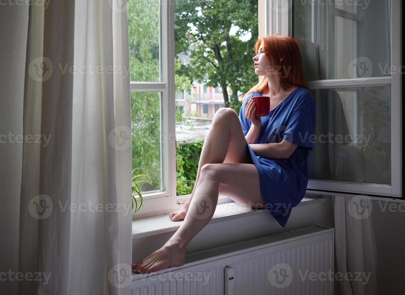 young woman with coffee mug sitting on window sill at home photo