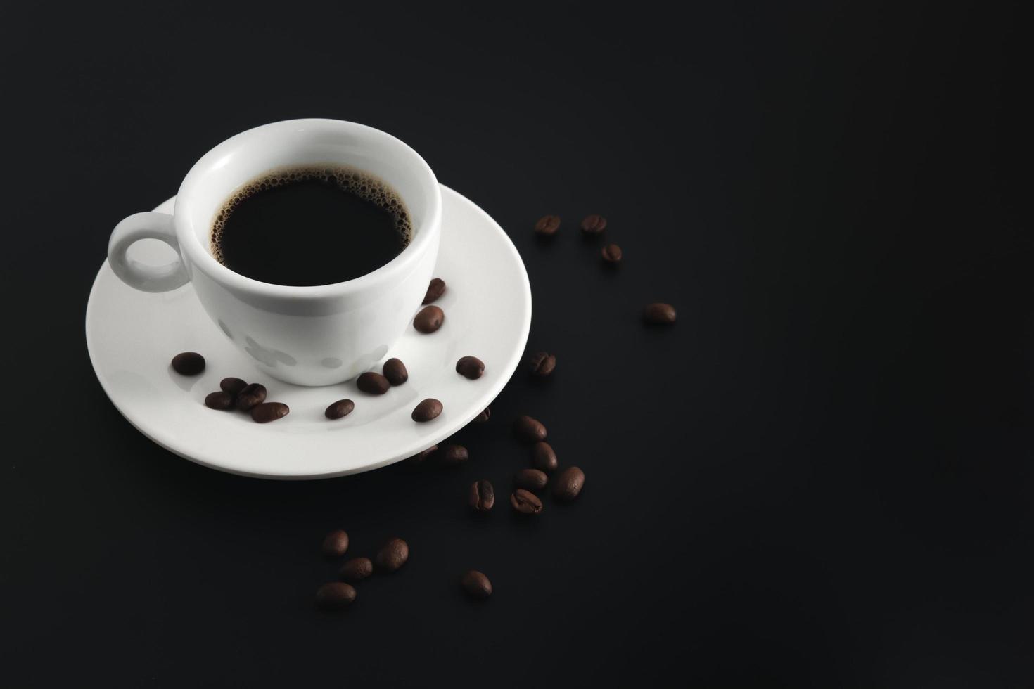 Black coffee in white coffee cup and saucer with beans coffee on black background. photo