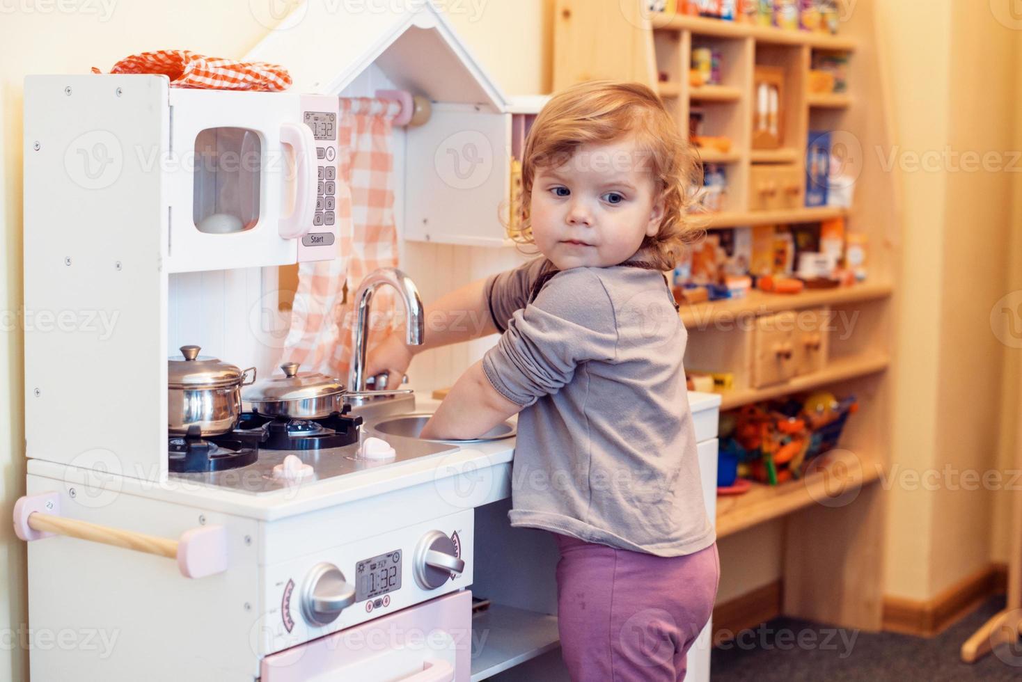 toddler girl playing toy kitchen photo