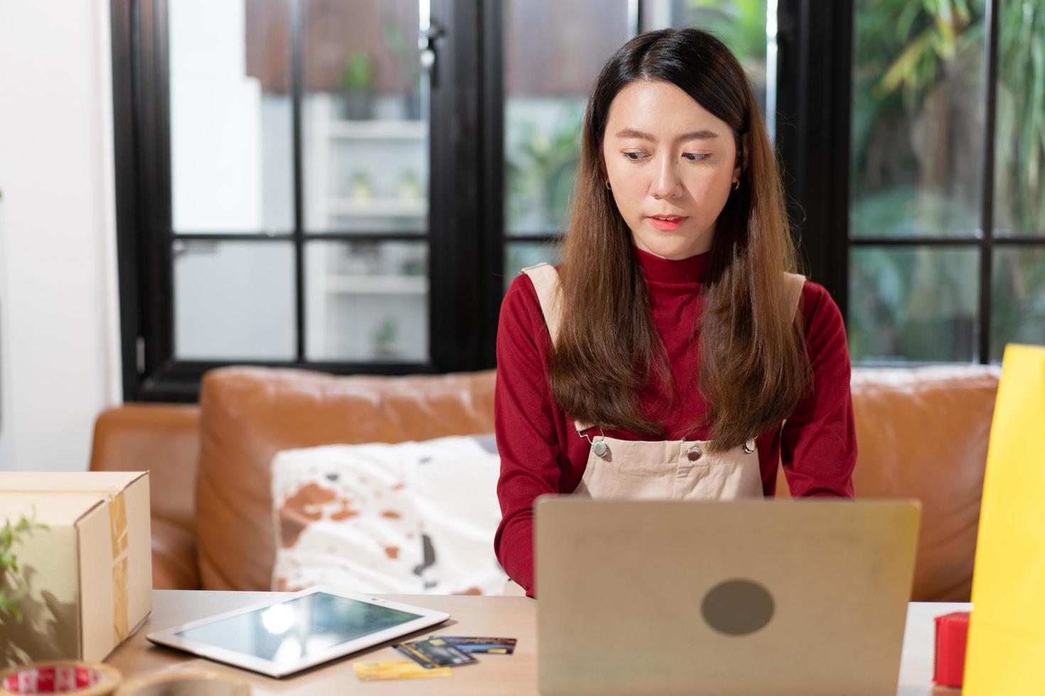 SME small business Asian female entrepreneur or shop owner using computer laptop checking on stock order. woman working for online store at home. management new normal lifestyle photo