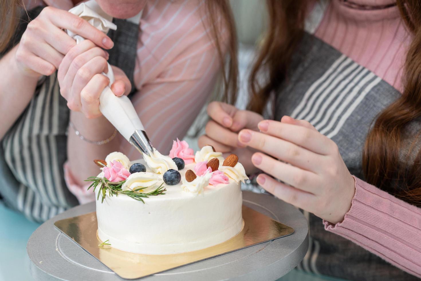 Hand of mother and daughter decorating topping on cake with whip cream. homemade bakery. family activity on weekend. photo