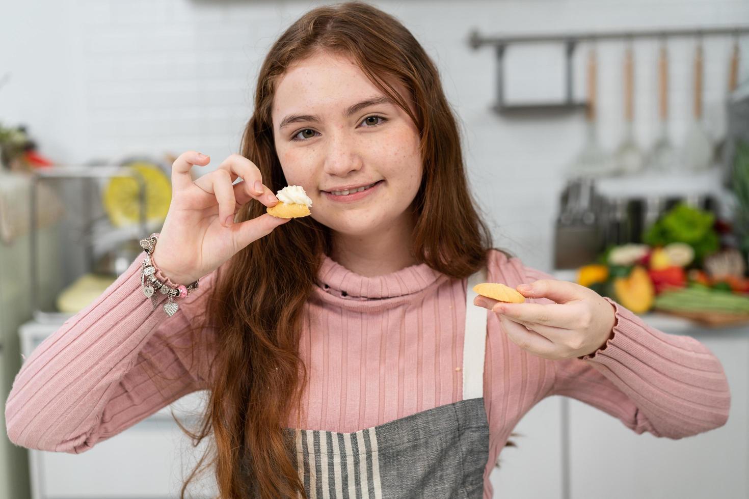 Caucasian girl in apron proud showing homemade cookies to camera. happy kid baking bakery in the kitchen on weekend. photo