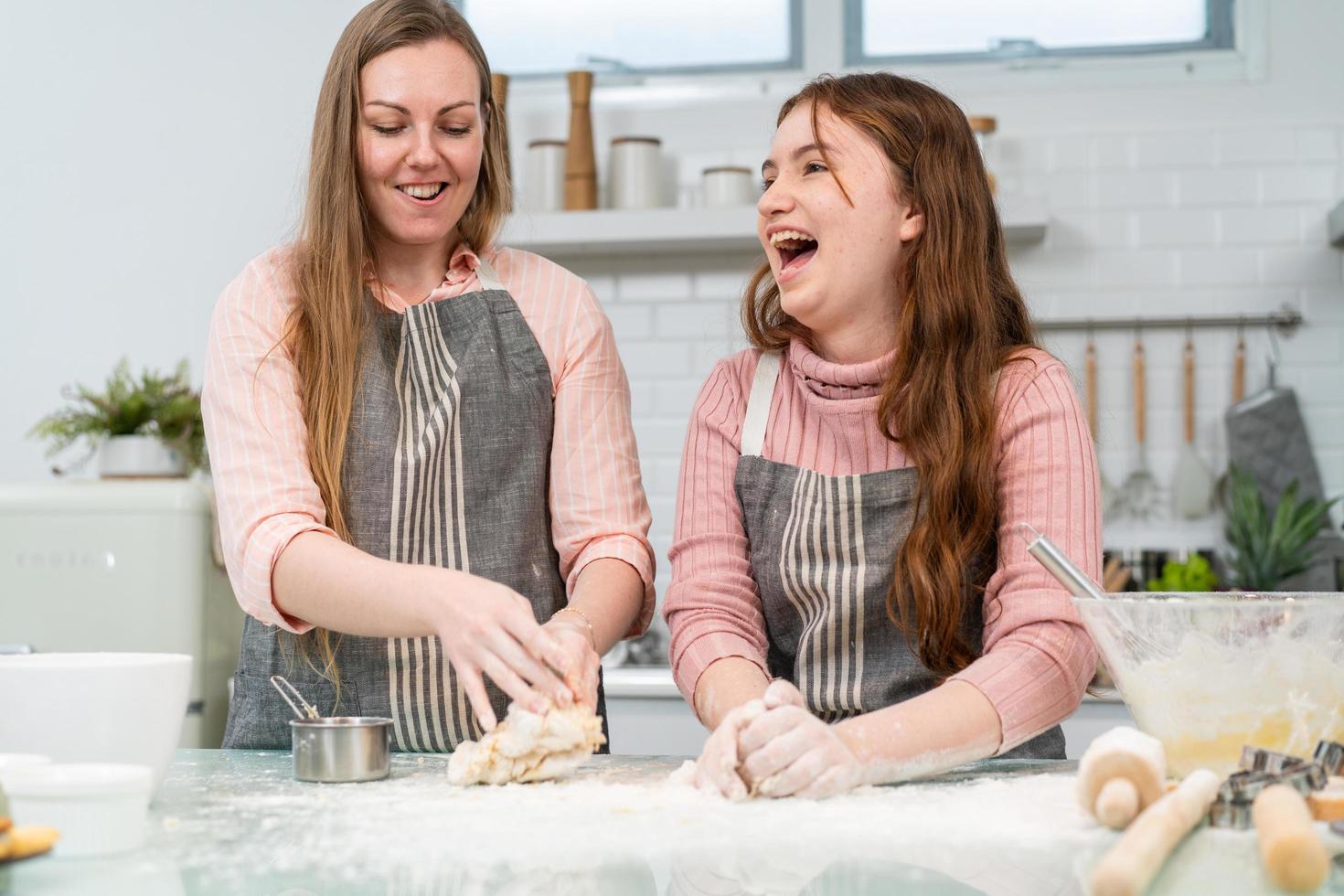 madre e hija disfrutan horneando panadería juntas en la cocina. sonriendo y riendo preparan recetas caseras. feliz actividad familiar el fin de semana. niño aprendiendo habilidades culinarias foto