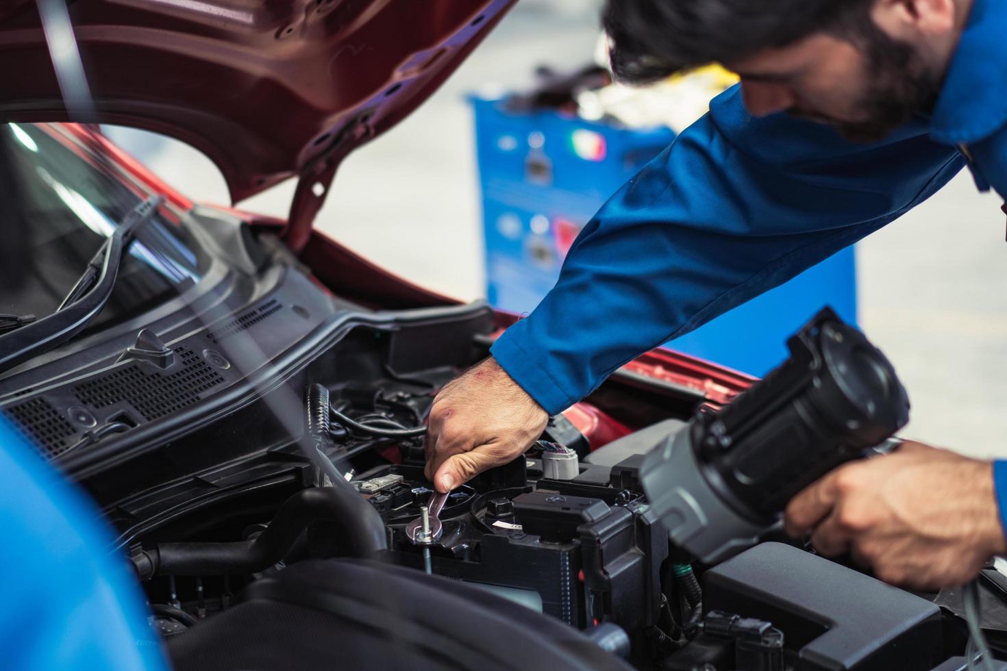 Male mechanic or technician holding flashlight and using wrench to repair in the car engine at auto repair shop. after service concept. photo