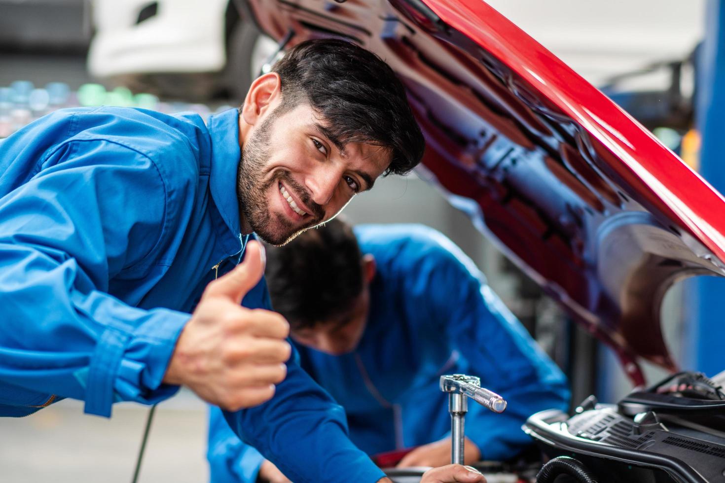 Happy smile Caucasian male mechanic showing thumbs up while checking car damage, diagnostic and repairing vehicle at garage automotive, motor technician maintenance after service concept photo