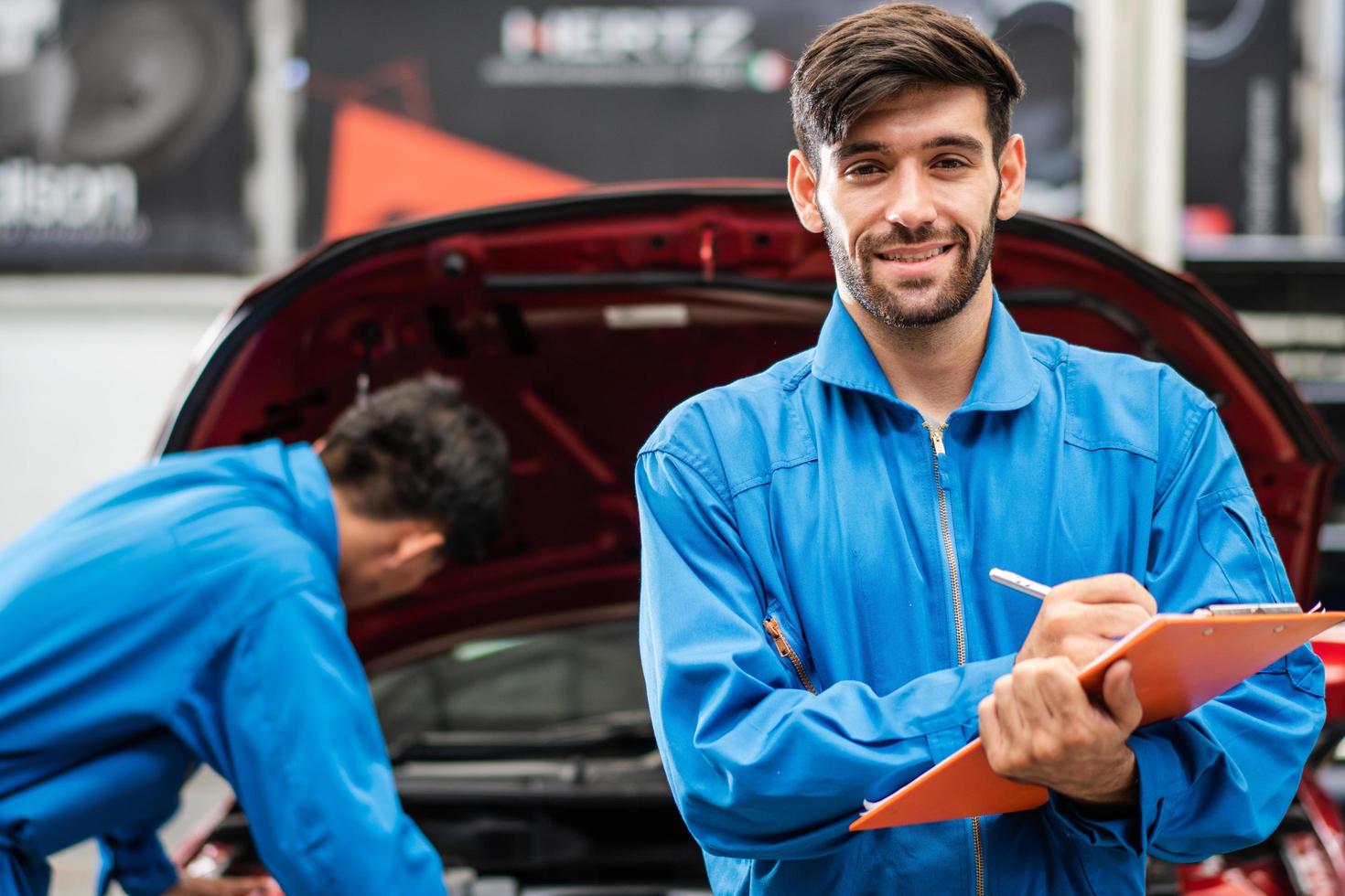 retrato de un mecánico automotriz caucásico escribiendo en el portapapeles de documentos de mantenimiento y revisando daños automáticos en el garaje de automóviles, asistente de reparación de automóviles, negocio de transporte y concepto de servicio posterior foto