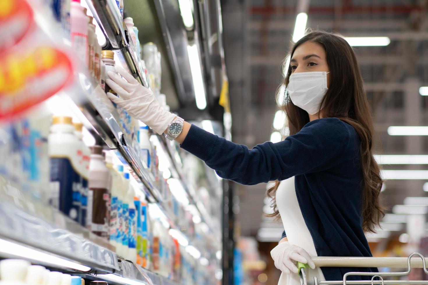 Woman wearing mask and rubber glove selecting product on shelf photo