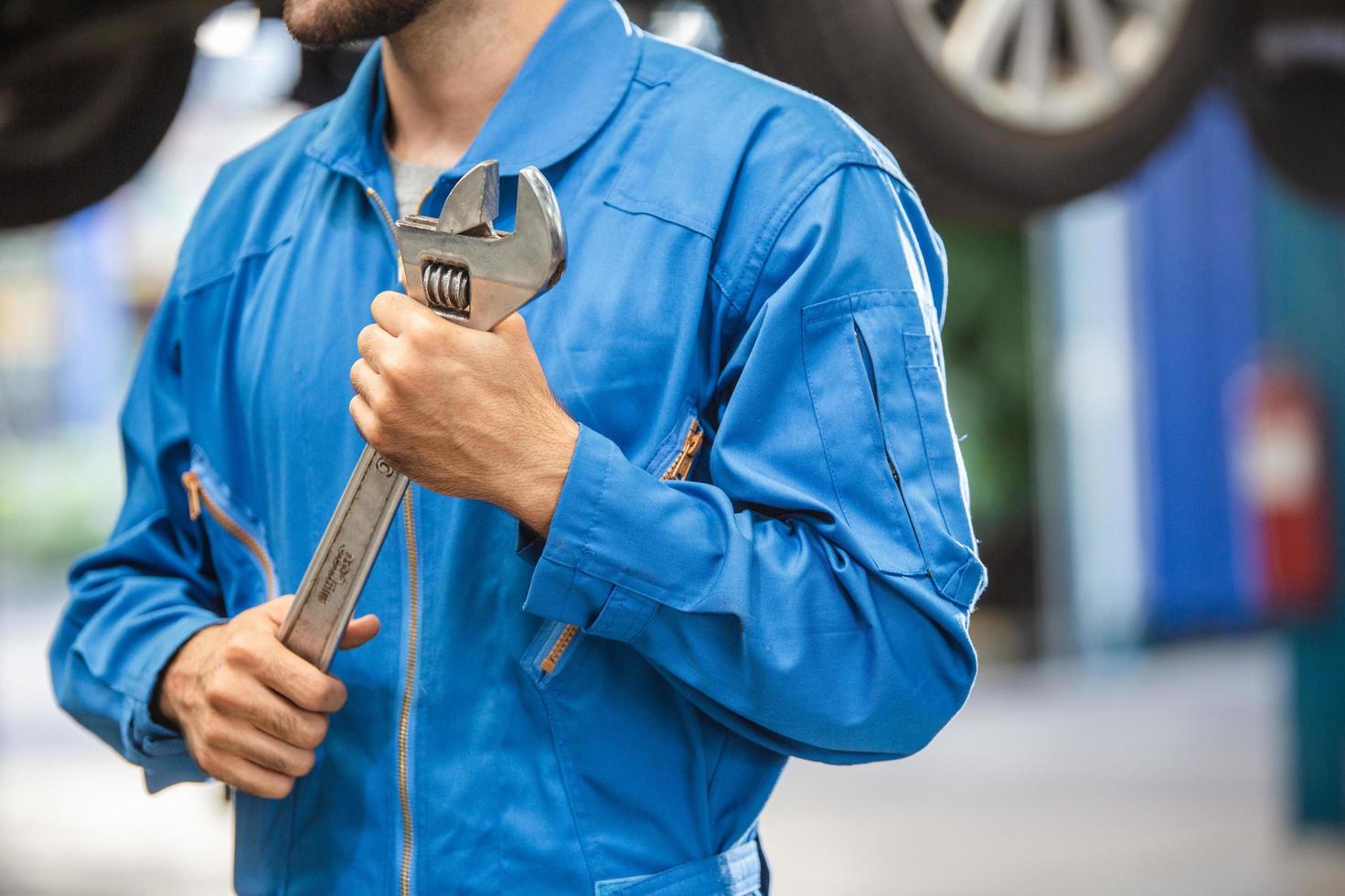 Mechanic hand holding wrench equipment tool in auto repair garage. checking car damage broken, repairing vehicle business. motor technician maintenance after service photo