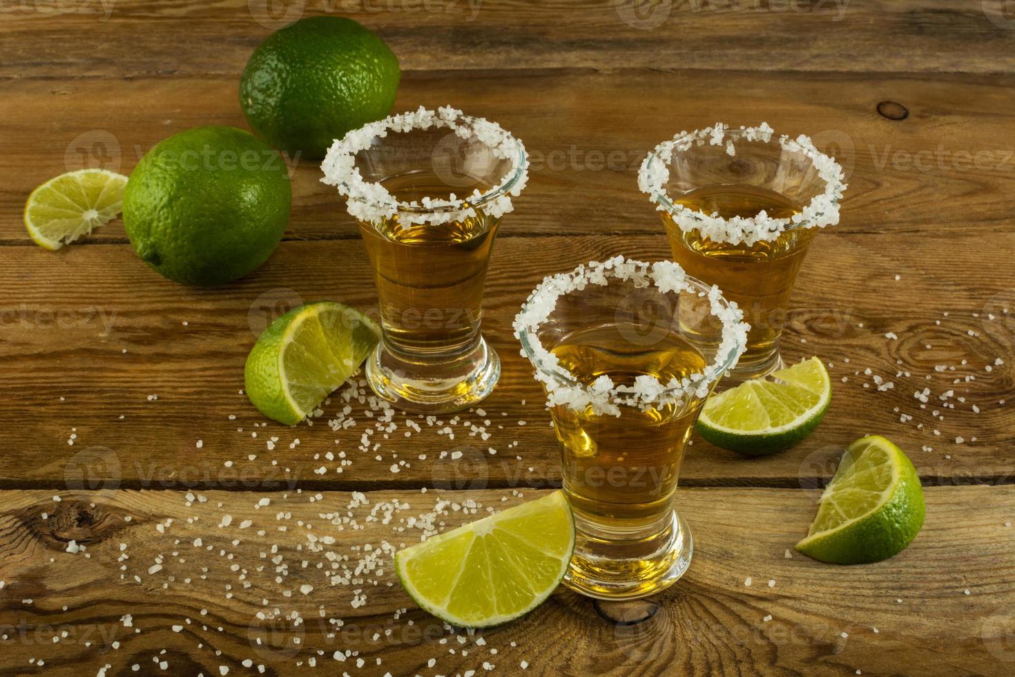 Three tequila shots with lime and salt on the wooden background photo