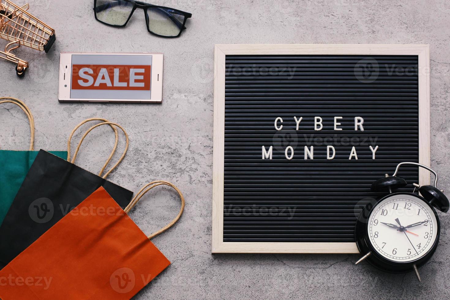 Creative flat lay promotion composition Cyber Monday sale text on letter board with alarm clock goodie bag and gadget photo