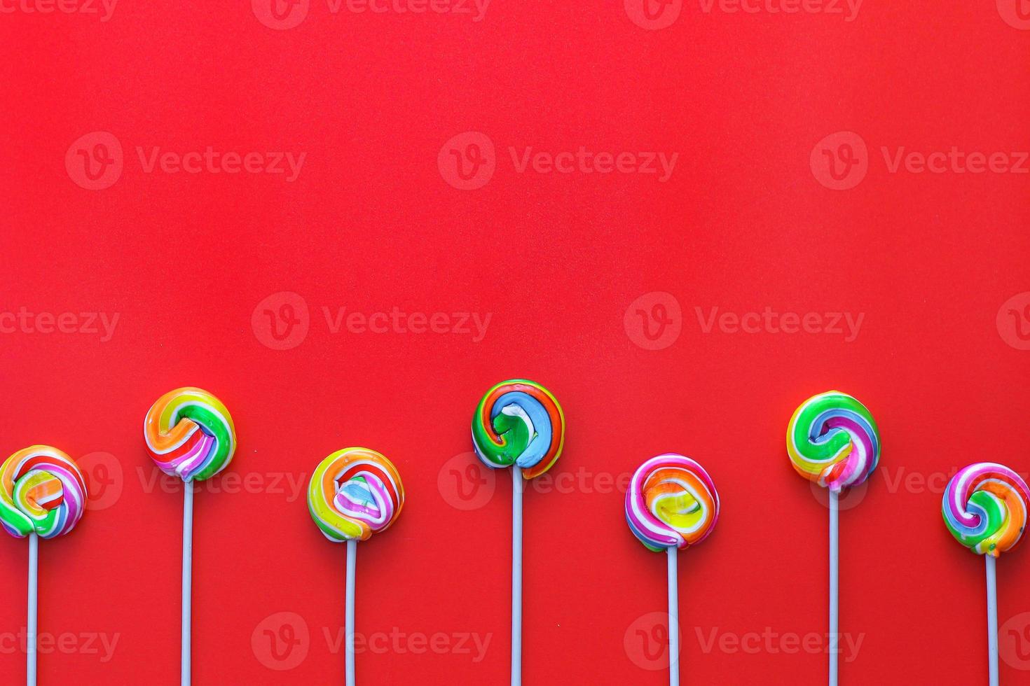 Creative flat lay of Rows of colorful lollipops on a red background with copy space on top photo