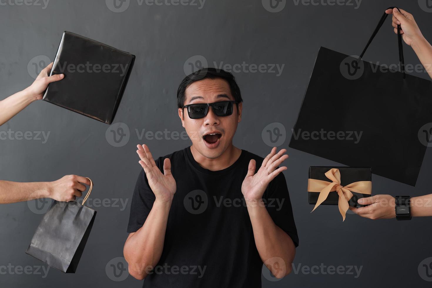 Shopaholic man surrounded by many hands holding shopping bags  with shocked expression photo