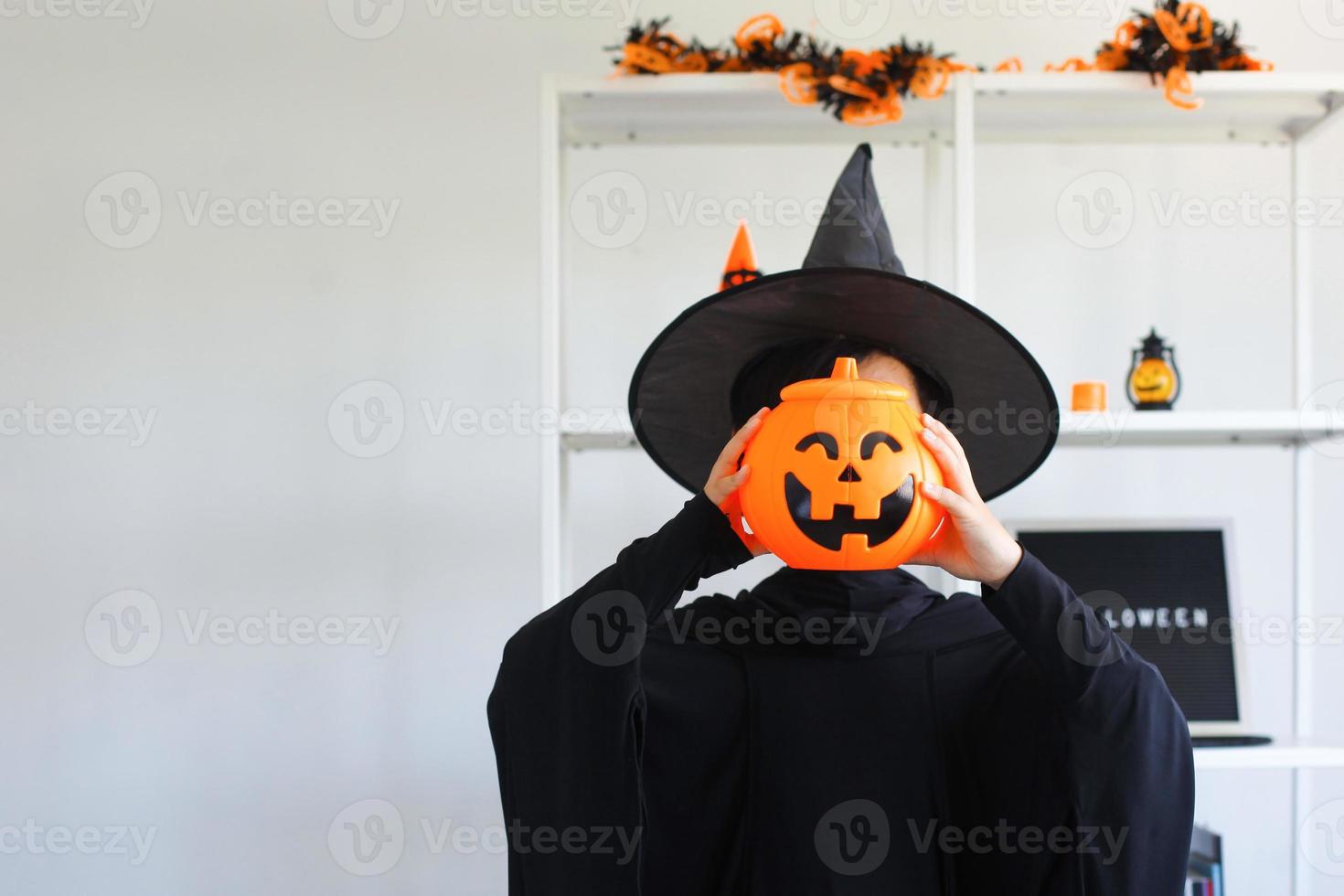 Cute Asian boy celebrating Halloween by wearing witch costume and holding Halloween decoration accessories photo