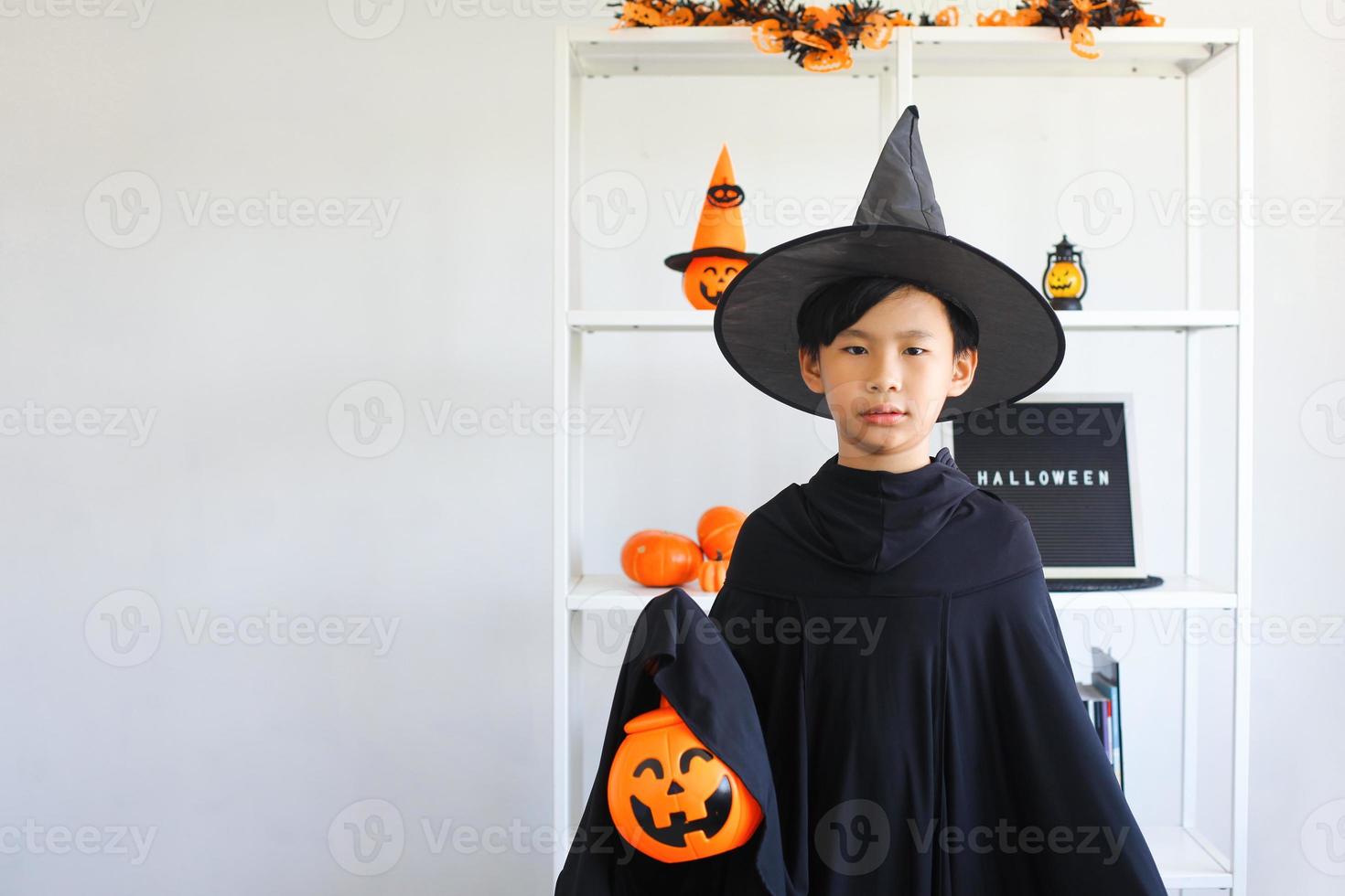 lindo niño asiático celebrando halloween vistiendo un disfraz de bruja y sosteniendo accesorios de decoración de halloween foto