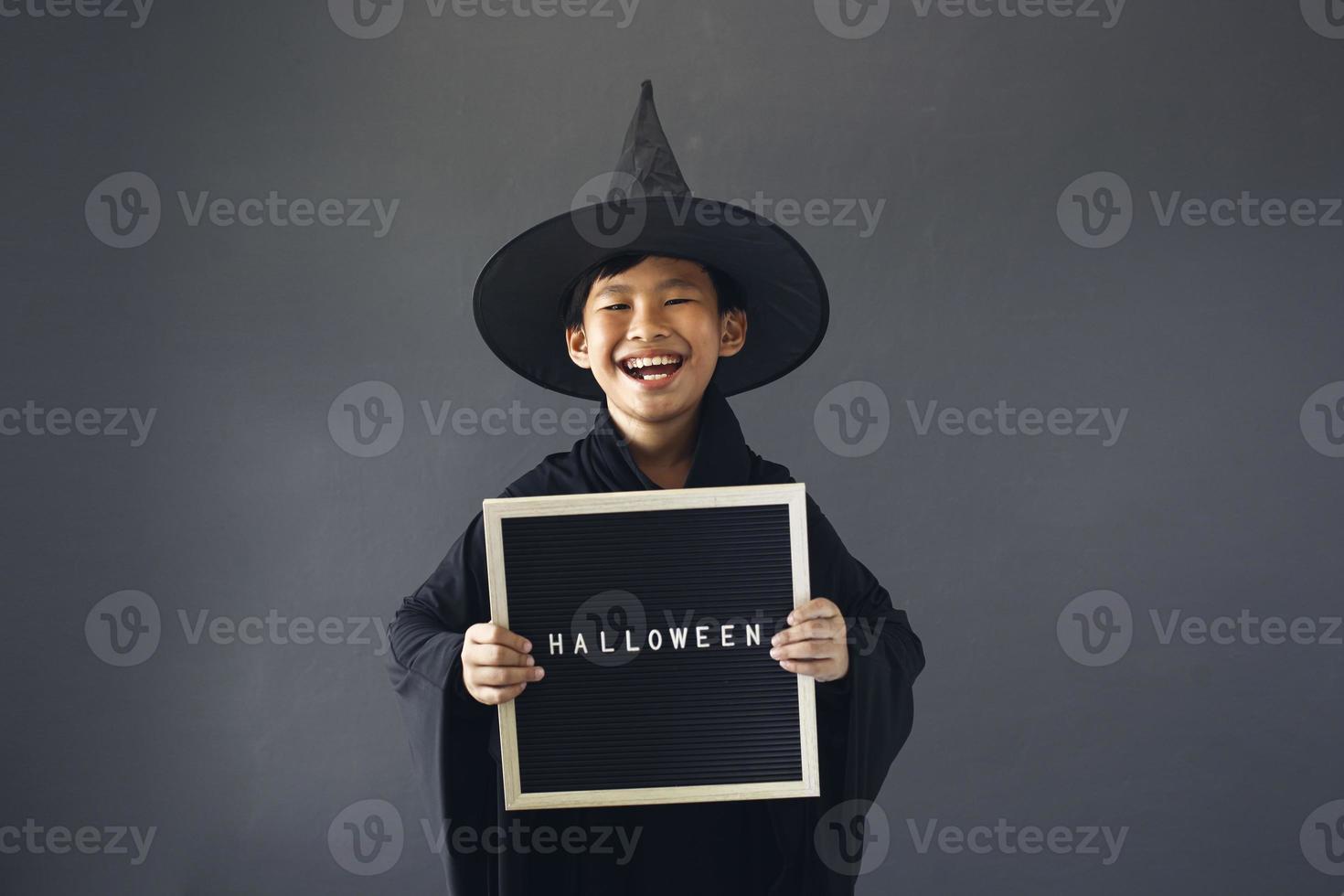 lindo niño asiático celebrando halloween vistiendo un disfraz de bruja y sosteniendo accesorios de decoración de halloween foto