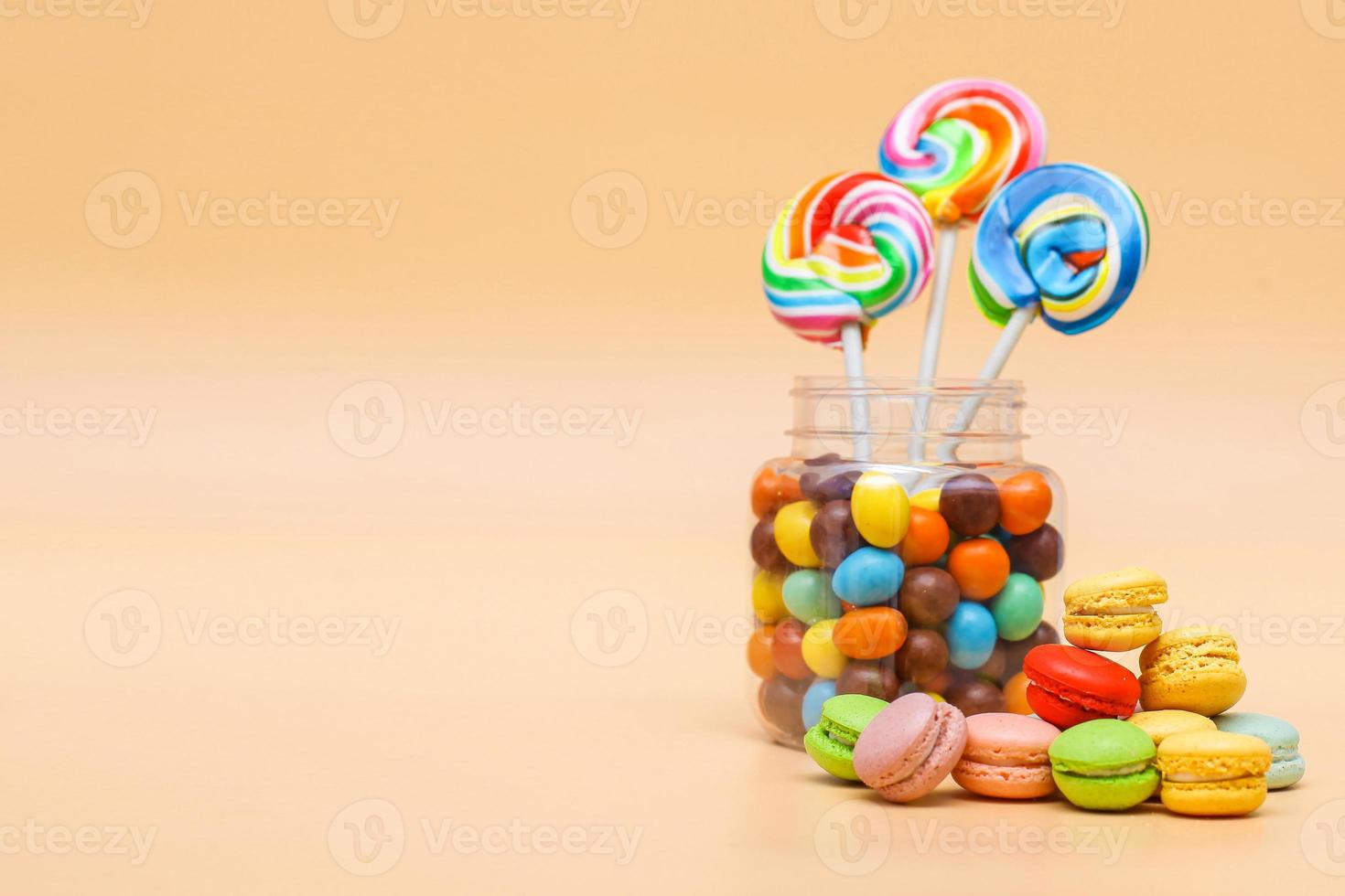 Assorted sweets in a jar and french macaroons cake on cream colored background with copy space photo