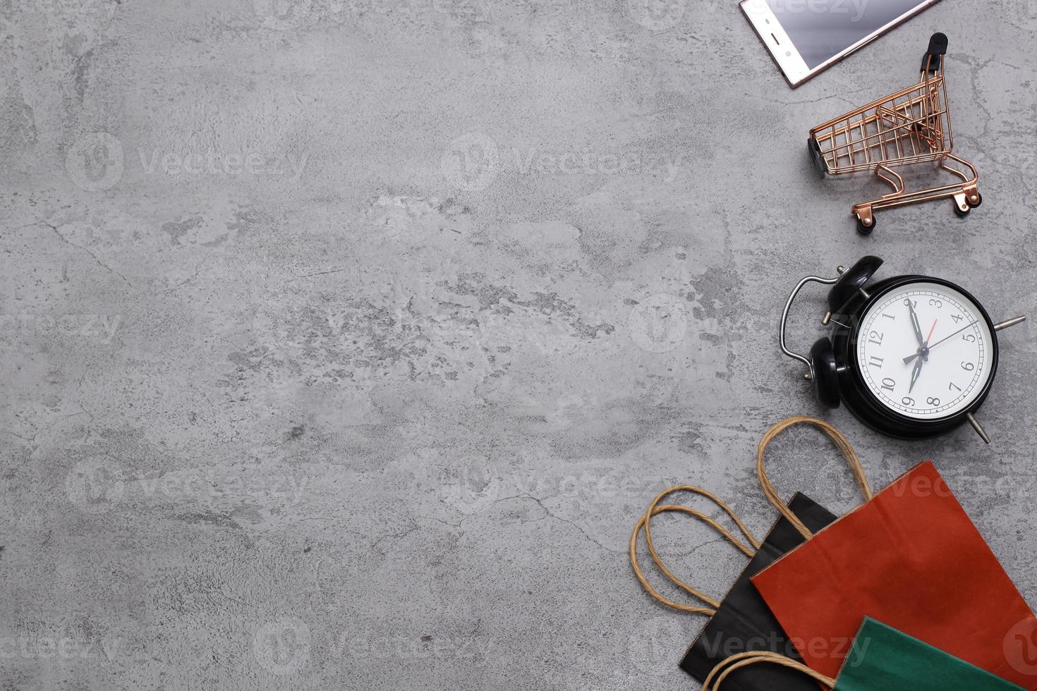 disposición plana de carrito de bolsas de compras y teléfono móvil sobre fondo gris ideas sobre el concepto de adicción a las compras en línea. foto