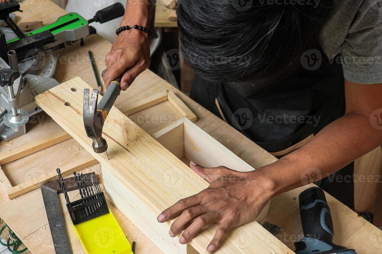 un joven carpintero trabajando en su mesa de taller usando un martillo foto