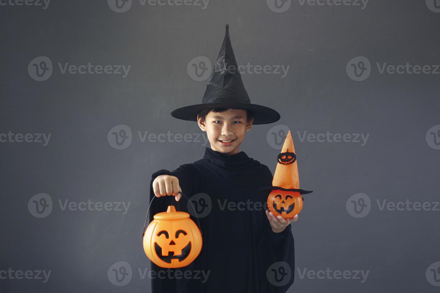 lindo niño asiático celebrando halloween vistiendo un disfraz de bruja y sosteniendo accesorios de decoración de halloween foto