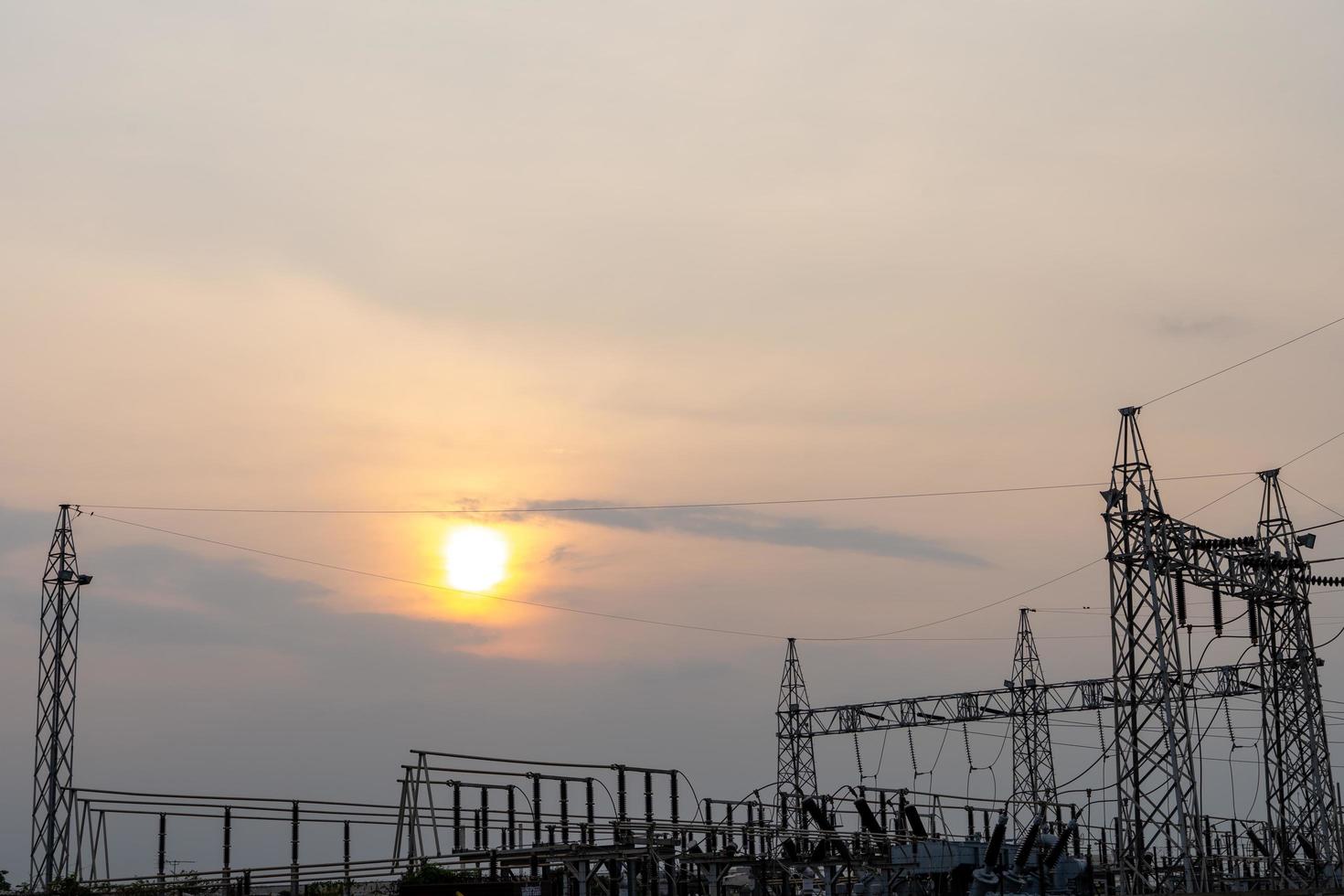 Photo of high-voltage steel poles at a power plant in the evening with the setting sun