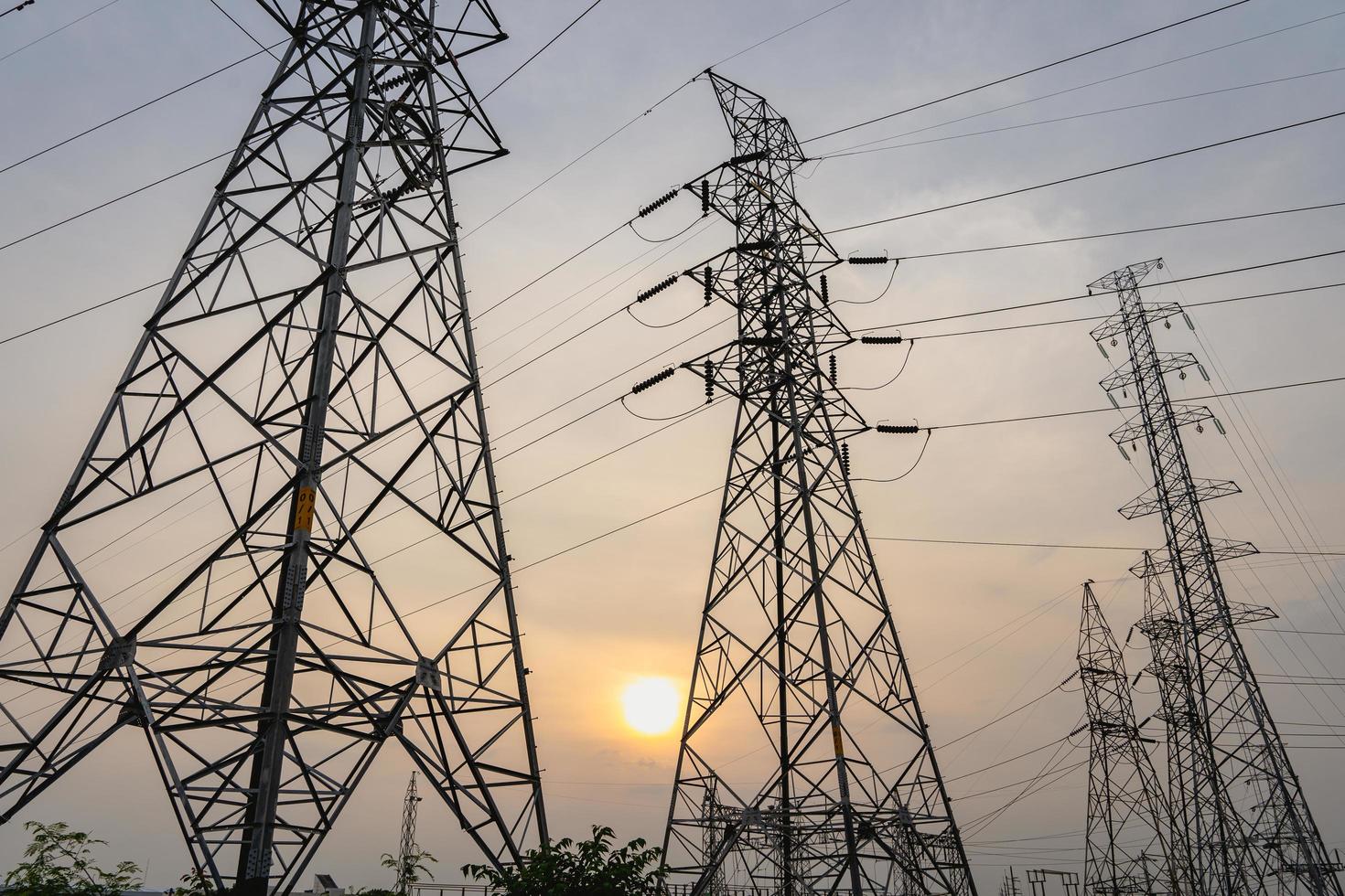 Photo of high-voltage steel poles at a power plant in the evening with the setting sun
