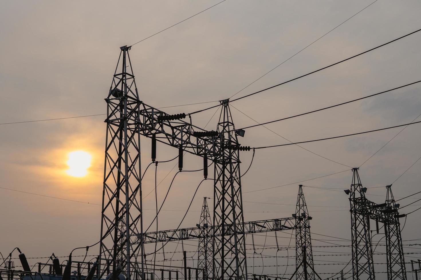 Photo of high-voltage steel poles at a power plant in the evening with the setting sun