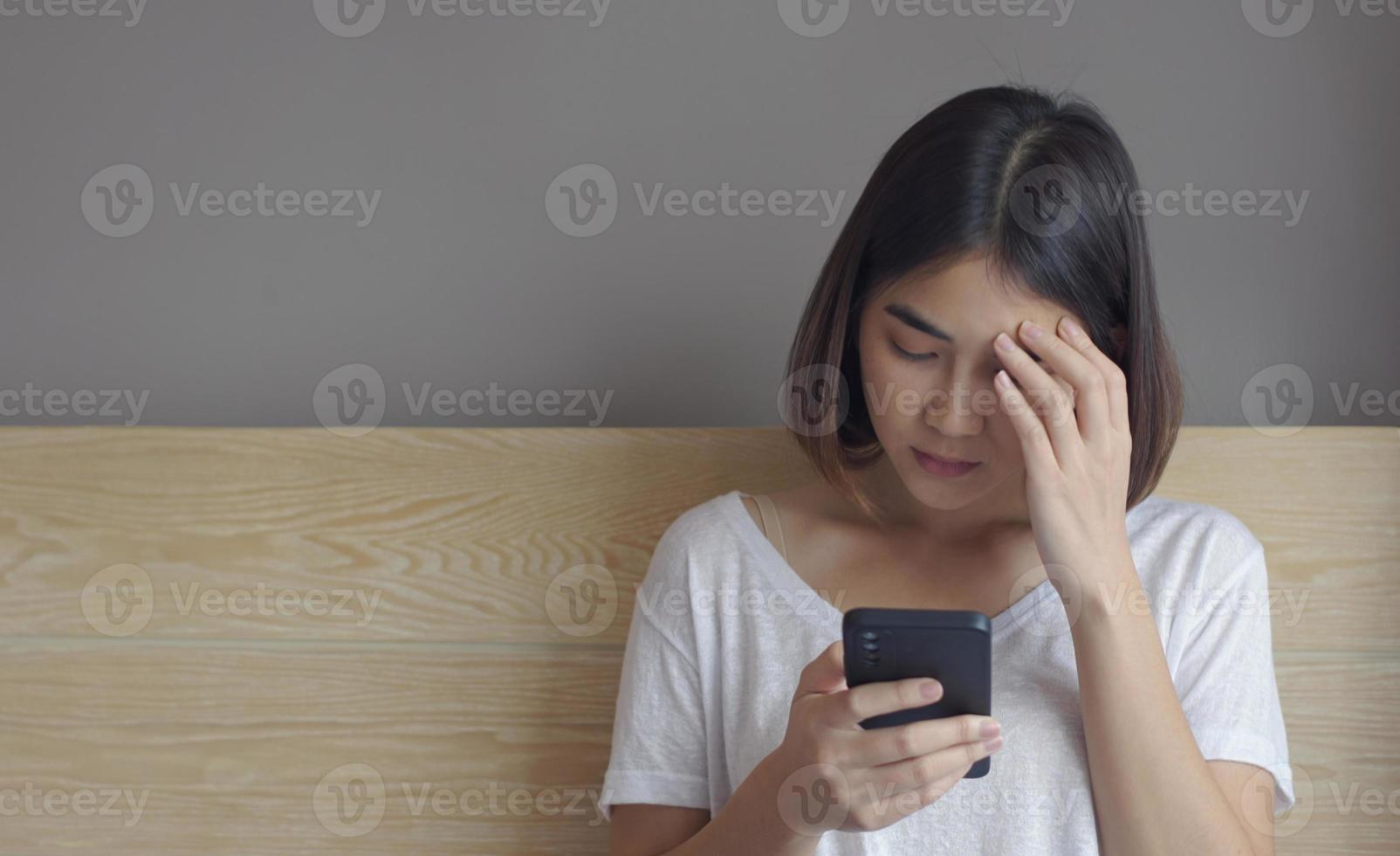 Upset young woman sitting on bed, holding smartphone in hands, received message with bad news. photo