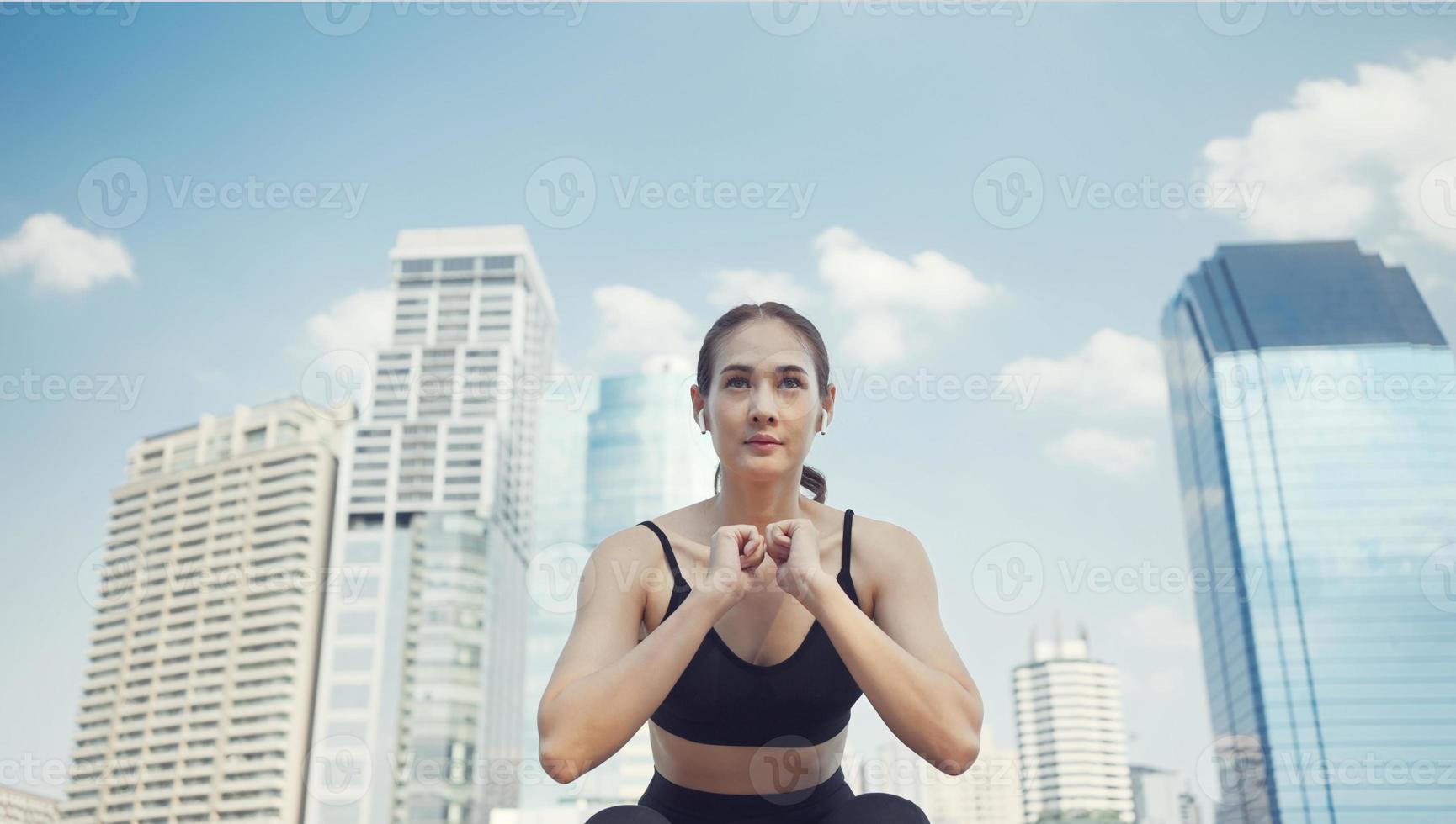 Sport woman squatting for warm up before fitness training. Athlete woman doing stretching exercise in city street near multistorey buildings. photo