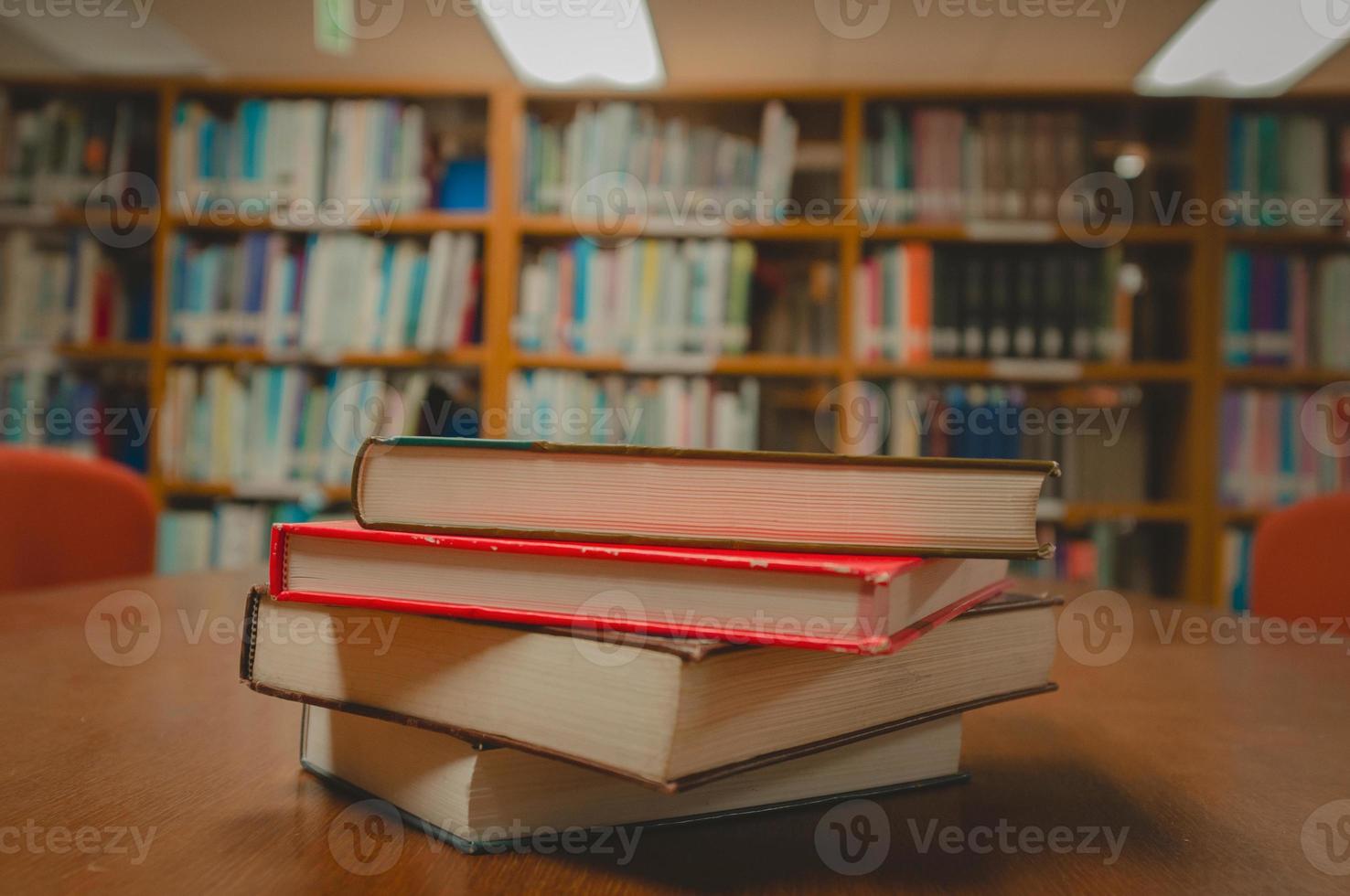 Stack of books on table and blurred bookshelf in the library room, education background. photo