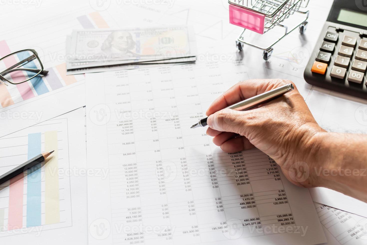 Financial accounting, work at home, Close-up Man's hand holding a pen examining accounting numbers. Numbers on paper and calculator, Many numbers, graph, pencil, glasses on paper, Blurred background. photo