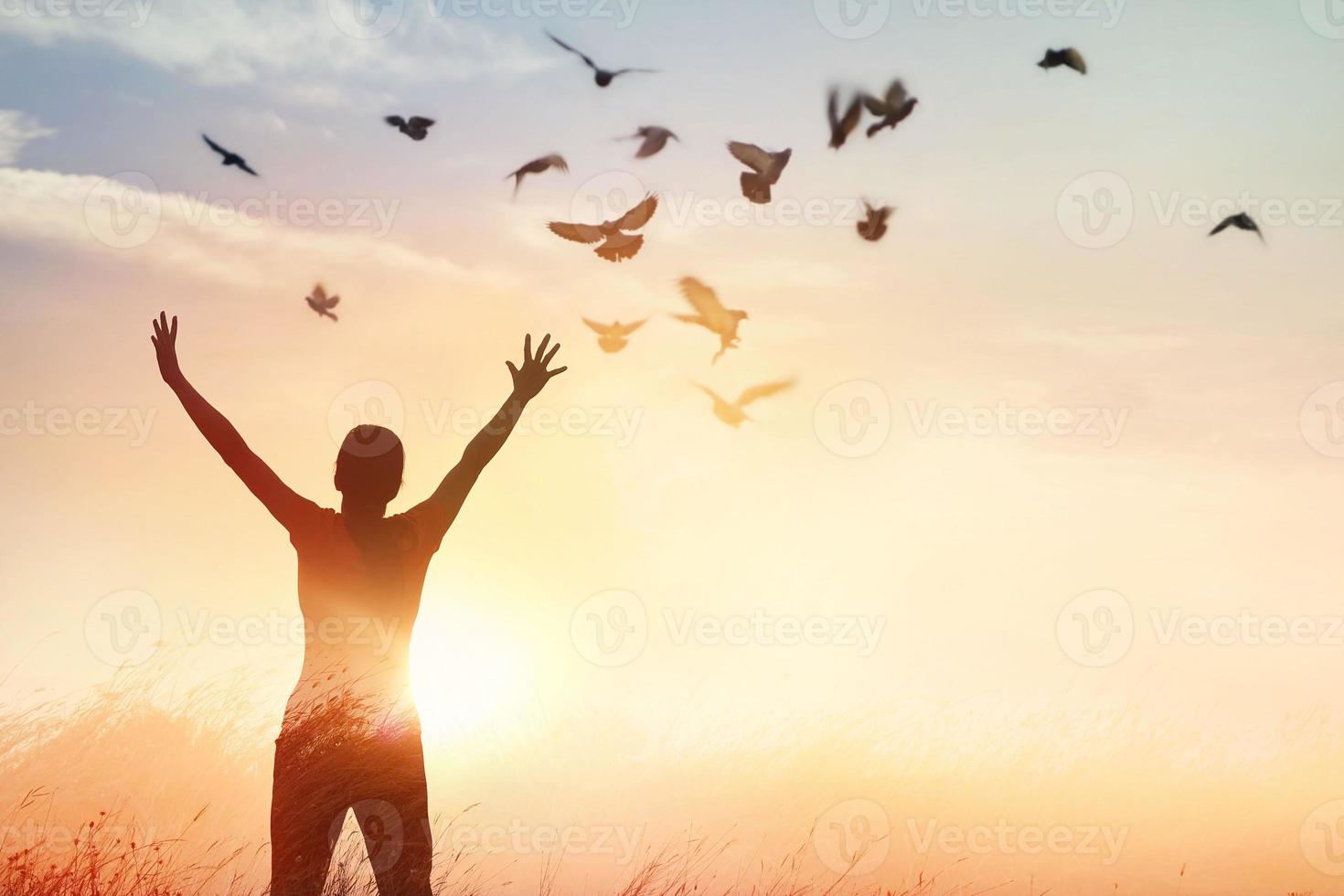 Woman praying and free bird enjoying nature on sunset background, hope concept photo
