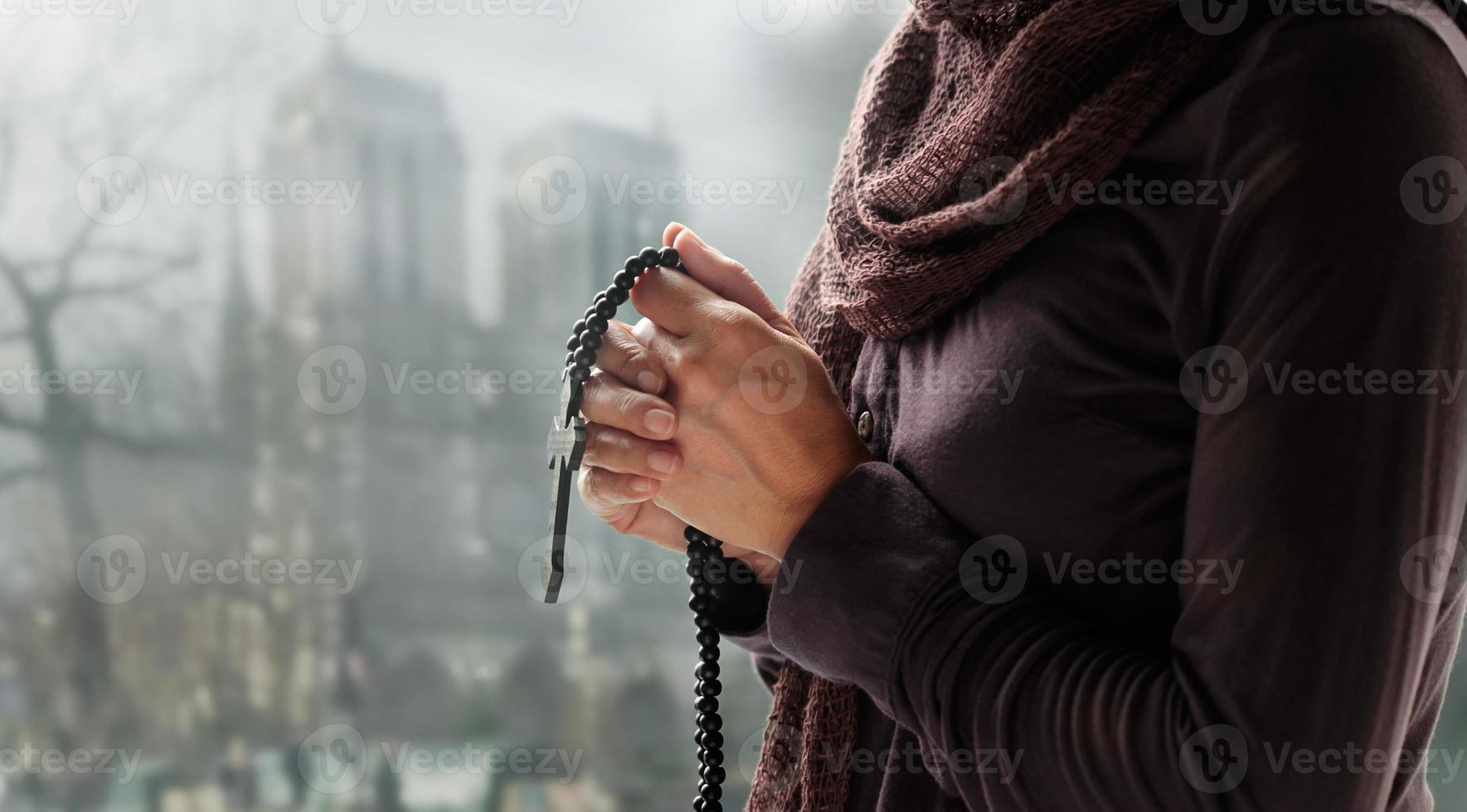 Woman praying with rosary and wooden cross on church background. Hope concept photo