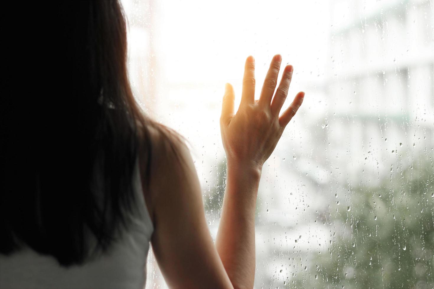 Sad woman looking through the glass window with a rain drops on city background photo